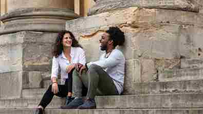 Two Rhodes Scholars are sitting on stone steps leaning against a large stone pillar