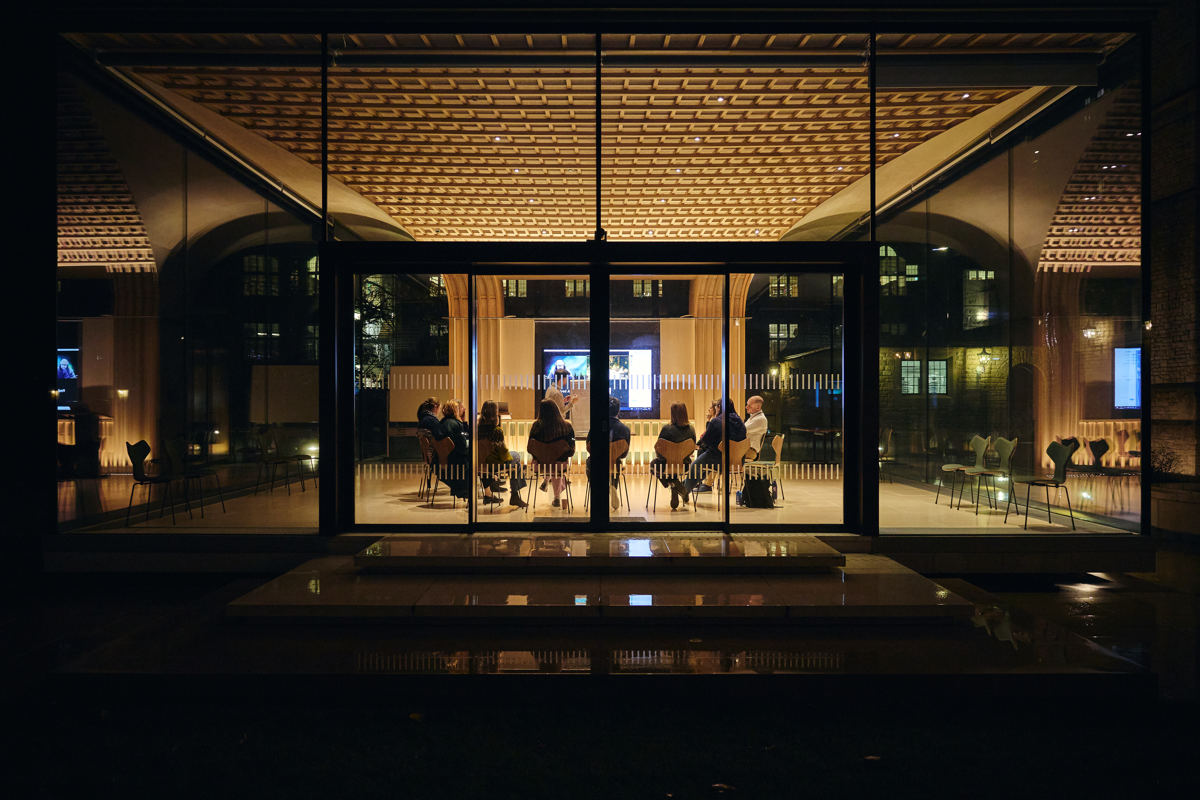 View of the Rhodes House Glass Pavilion at night with delegates in a meeting.