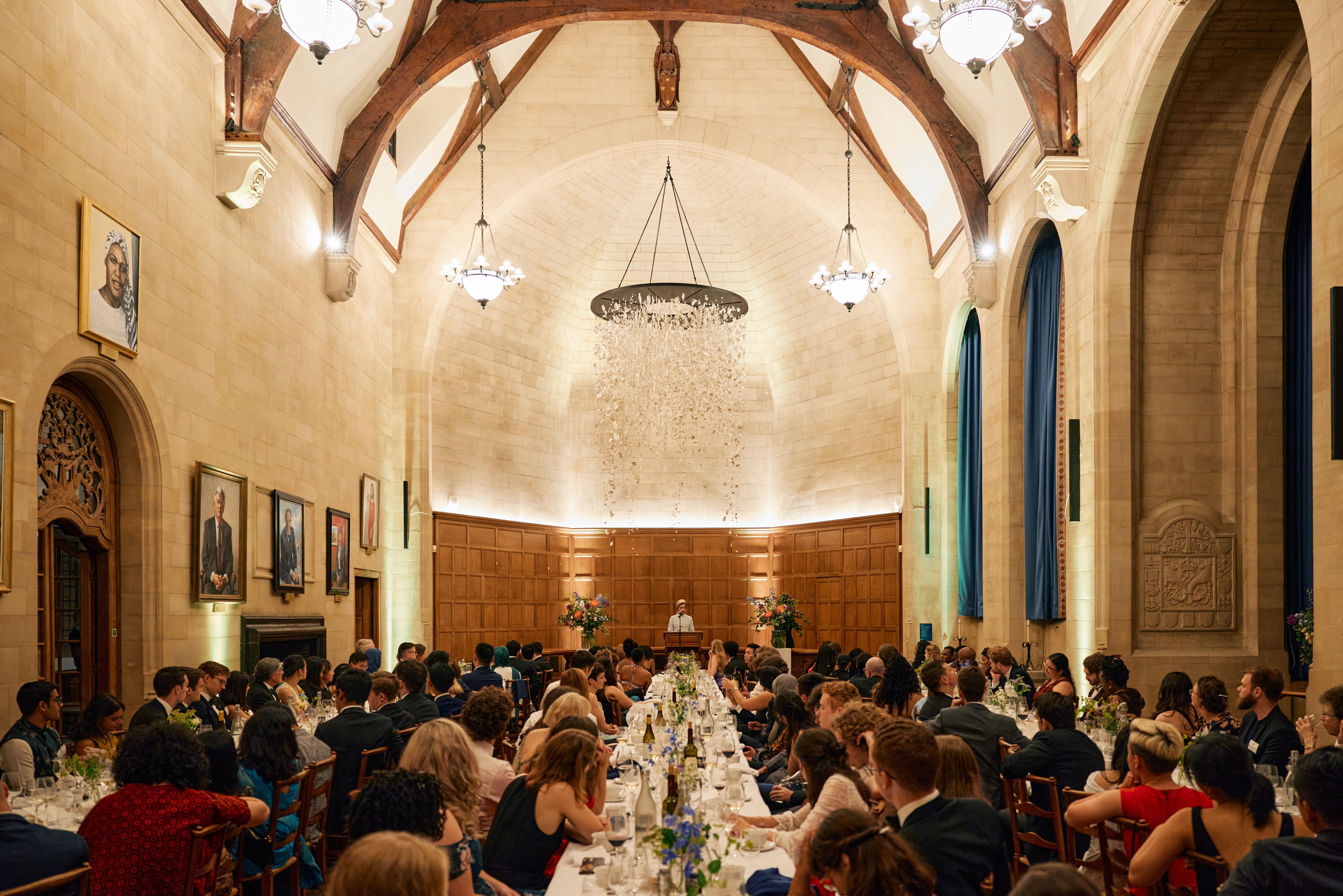 Dinner speaker speaking from lectern in Rhodes House McCall MacBain Hall with guests watching from banquet tables