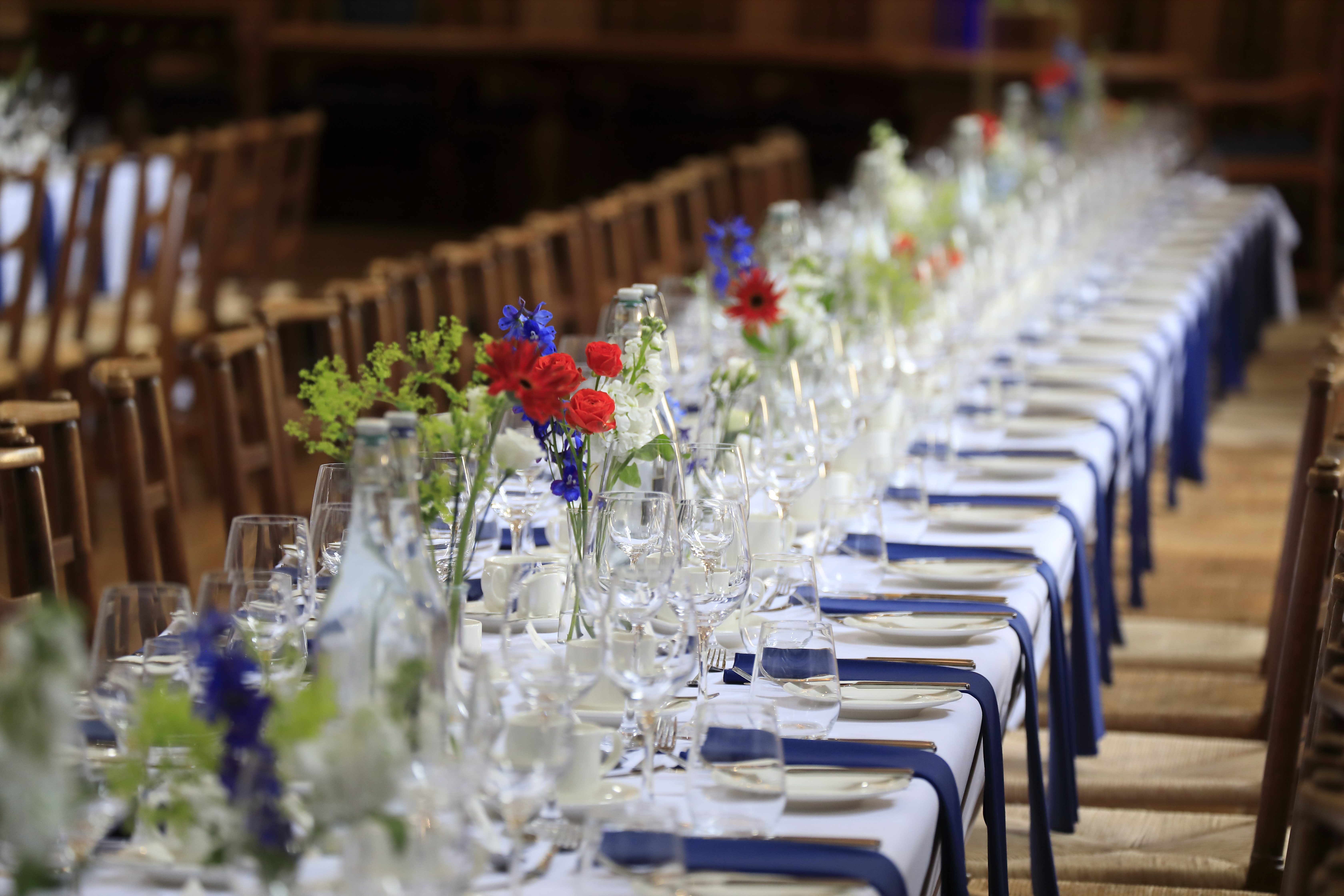 Rhodes House McCall MacBain Hall dining table with blue napkins and red & blue flowers