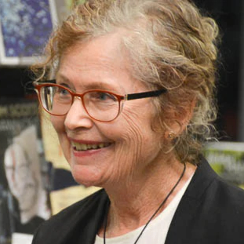 Close-up image of Elizabeth looking to the side and smiling. SHhe has her hair tied up and is wearing red glasses.