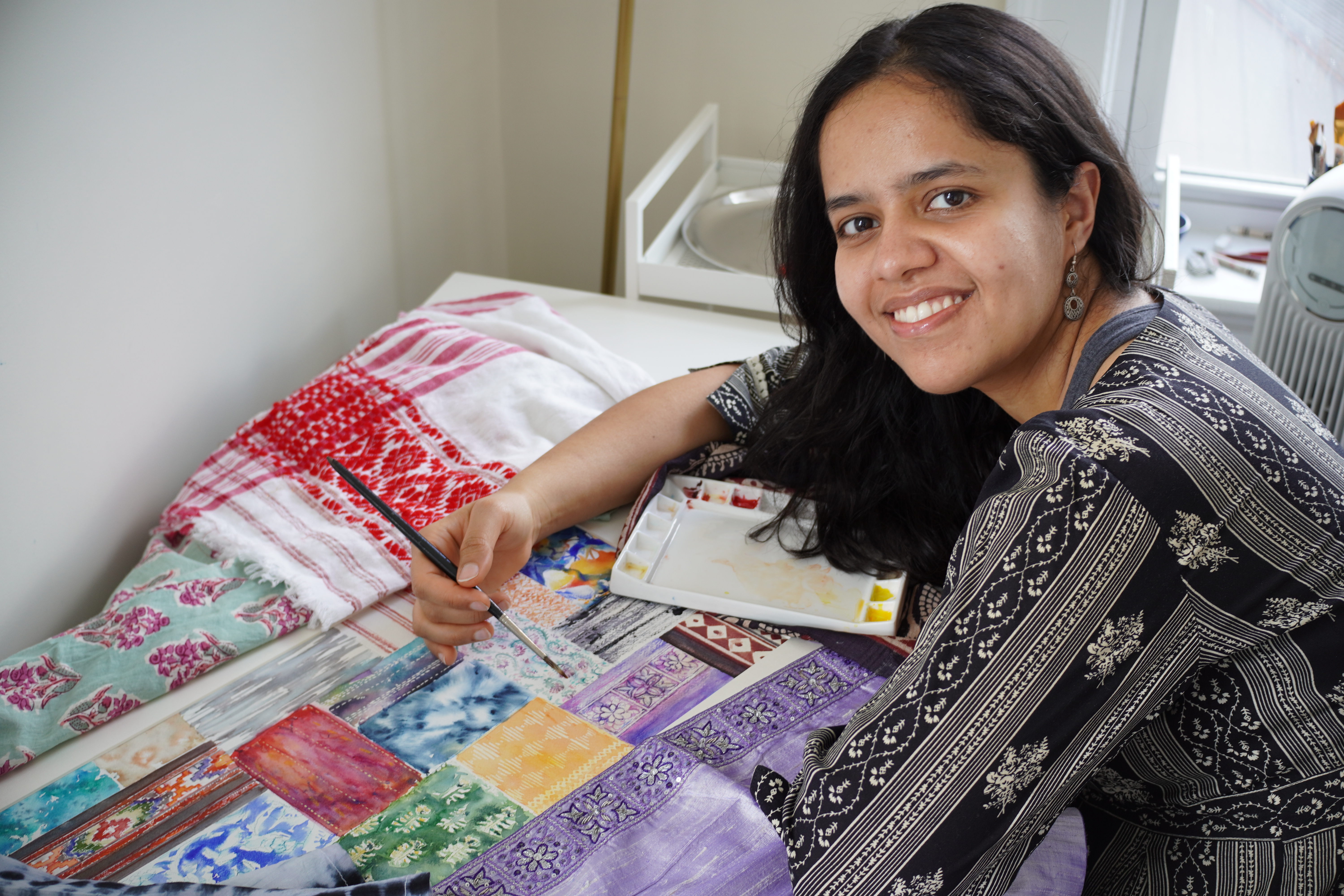 Mansi holding a paintbrush next to some printed fabrics