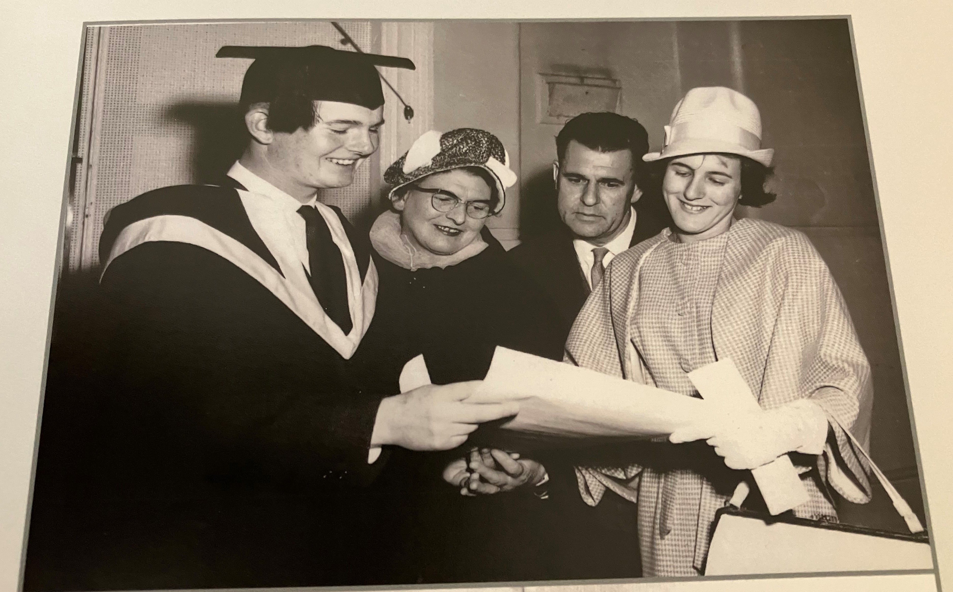 A black-and-white picture of Nick in a graduation gown. He is standing with his sister, mom and dad.