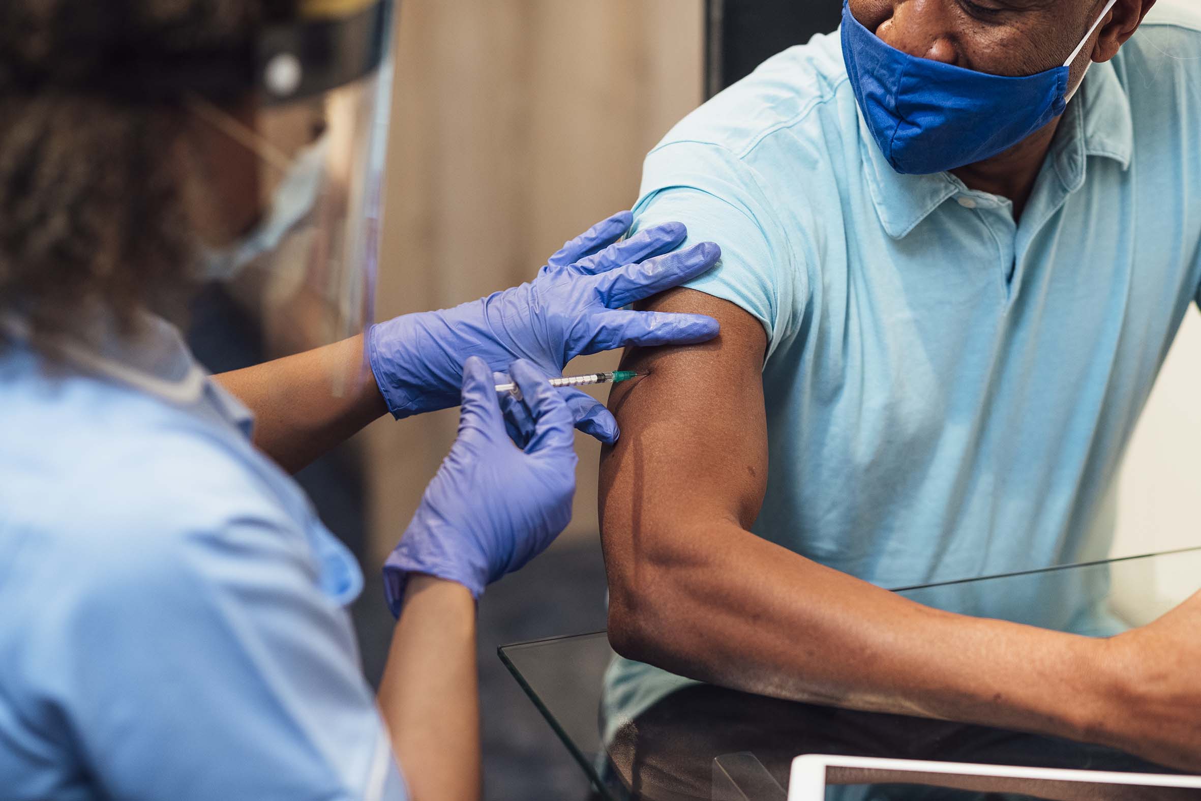 Someone vaccinating a patient wearing a blue tshirt.