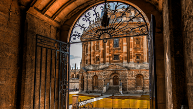 The Radcliffe Camera pictured from an iron gate doorway, and the sun is shining.