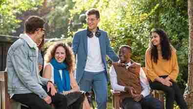 A group of six Rhodes Scholars talking in the Rhodes gardens on a summery day.