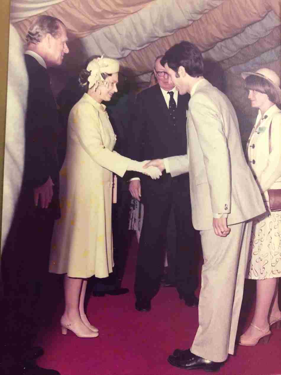 A portrait photograph shows Julian Heyes shaking hands with the Queen. Prince Philip and Julian’s wife Jane look on, smiling.