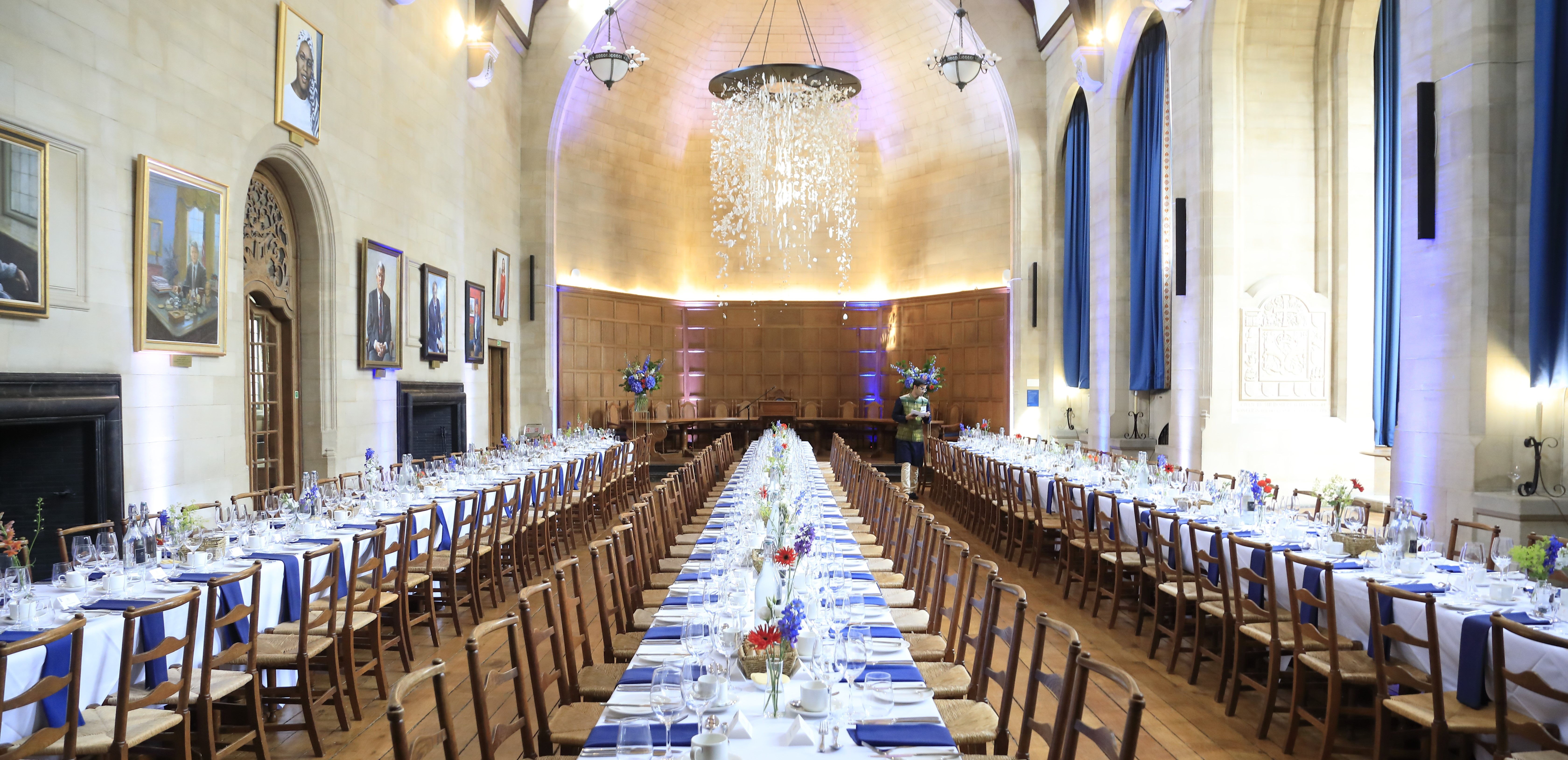 Rhodes House McCall MacBain Hall set up banquet style with blue napkins and red and blue flowers on the tables.