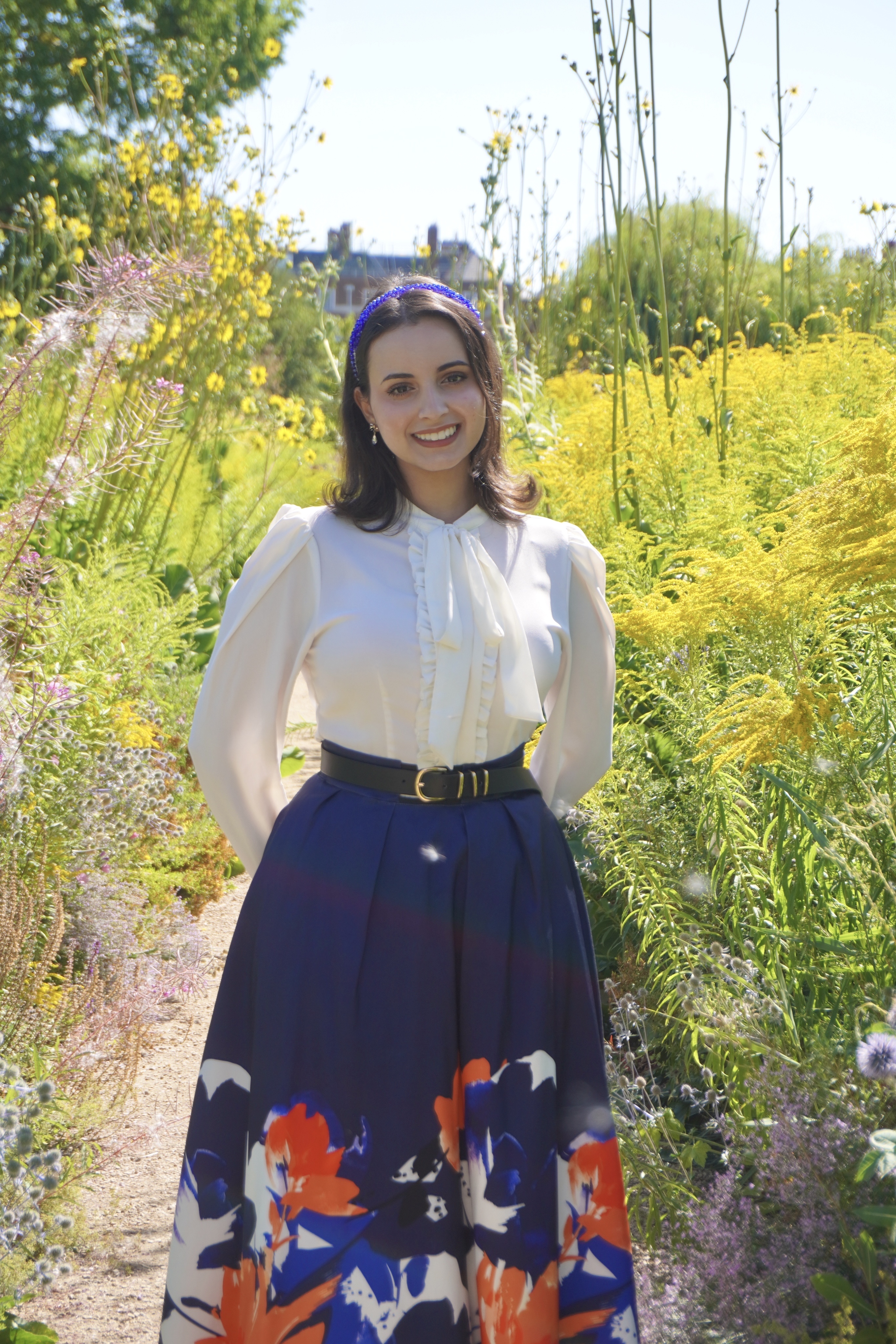 Lana standing in a field with tall flowers and a building behind her