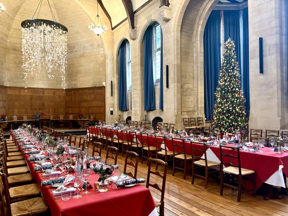 Two long banquet tables in Rhodes House McCall MacBain Hall set for Christmas dinner with a Christmas tree in the bay window