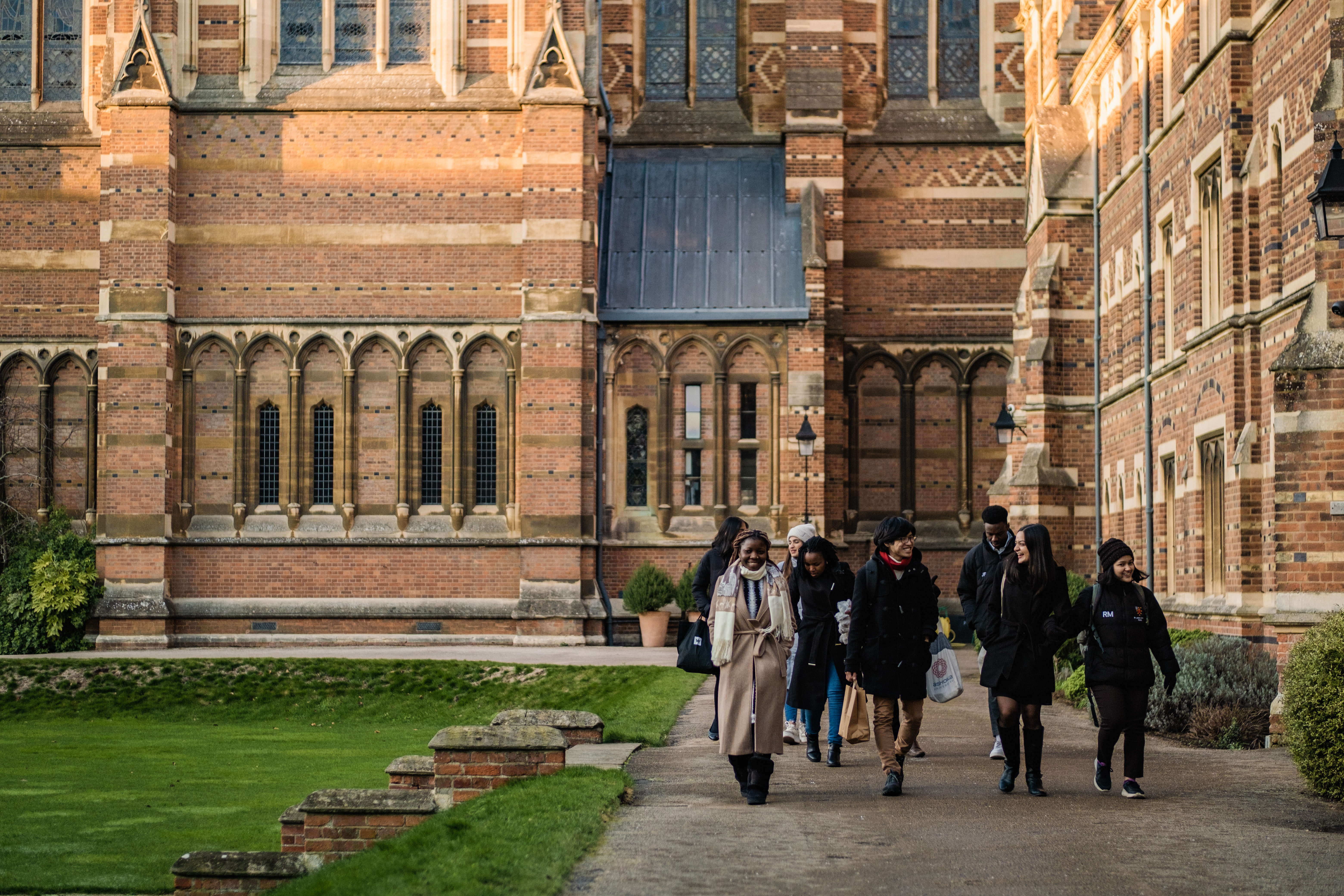 A group of students walking around in Oxford. There is an Oxford college with brickwork patterns in the background.