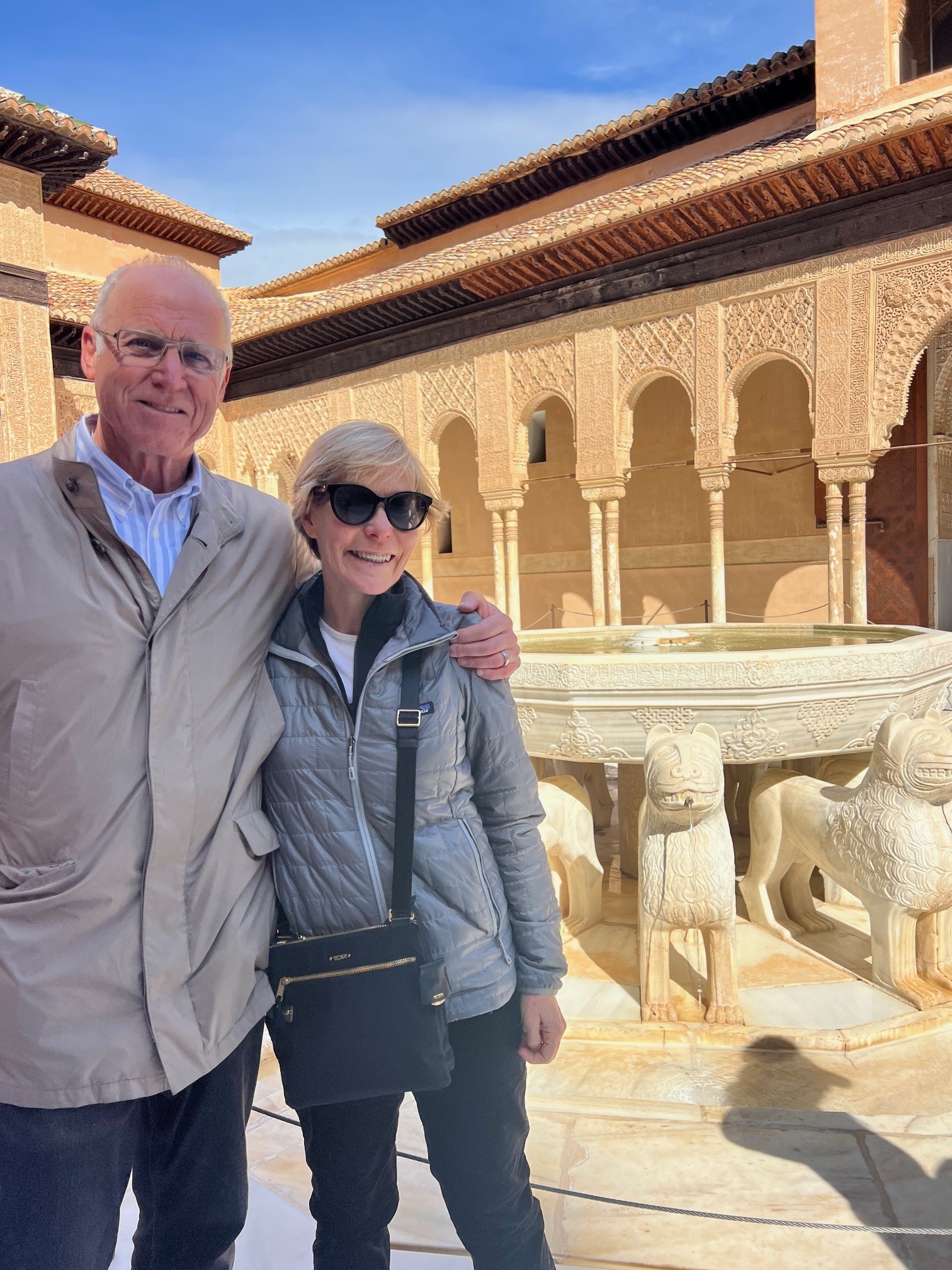 Mary with a man holding her shoulders. In the background is a sandstone building with delicate pillars and a fountain.