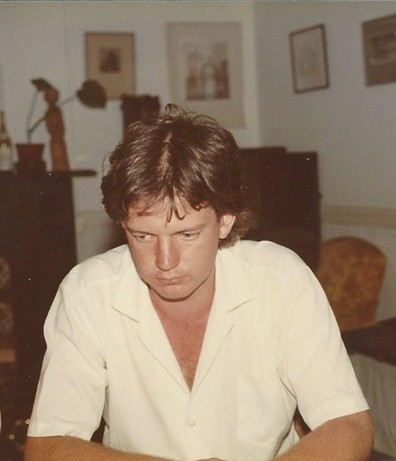 A photograph of Malcolm as a younger man sat in what appears to be a living room. He is looking down at the floor, deep in thought.