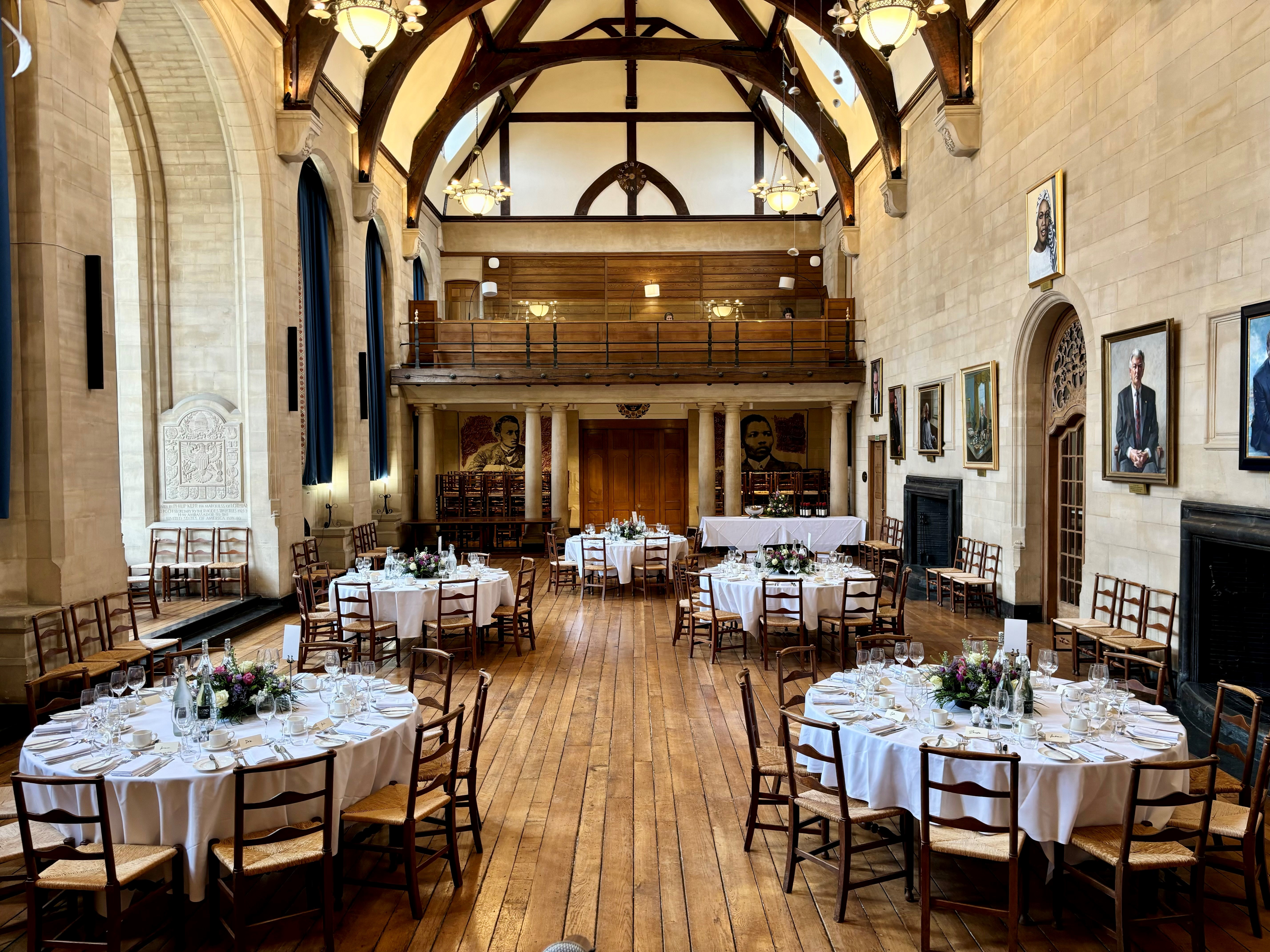 Rhodes House McCall MacBain Hall set up for a served dinner with round dining tables laid with white cloths.