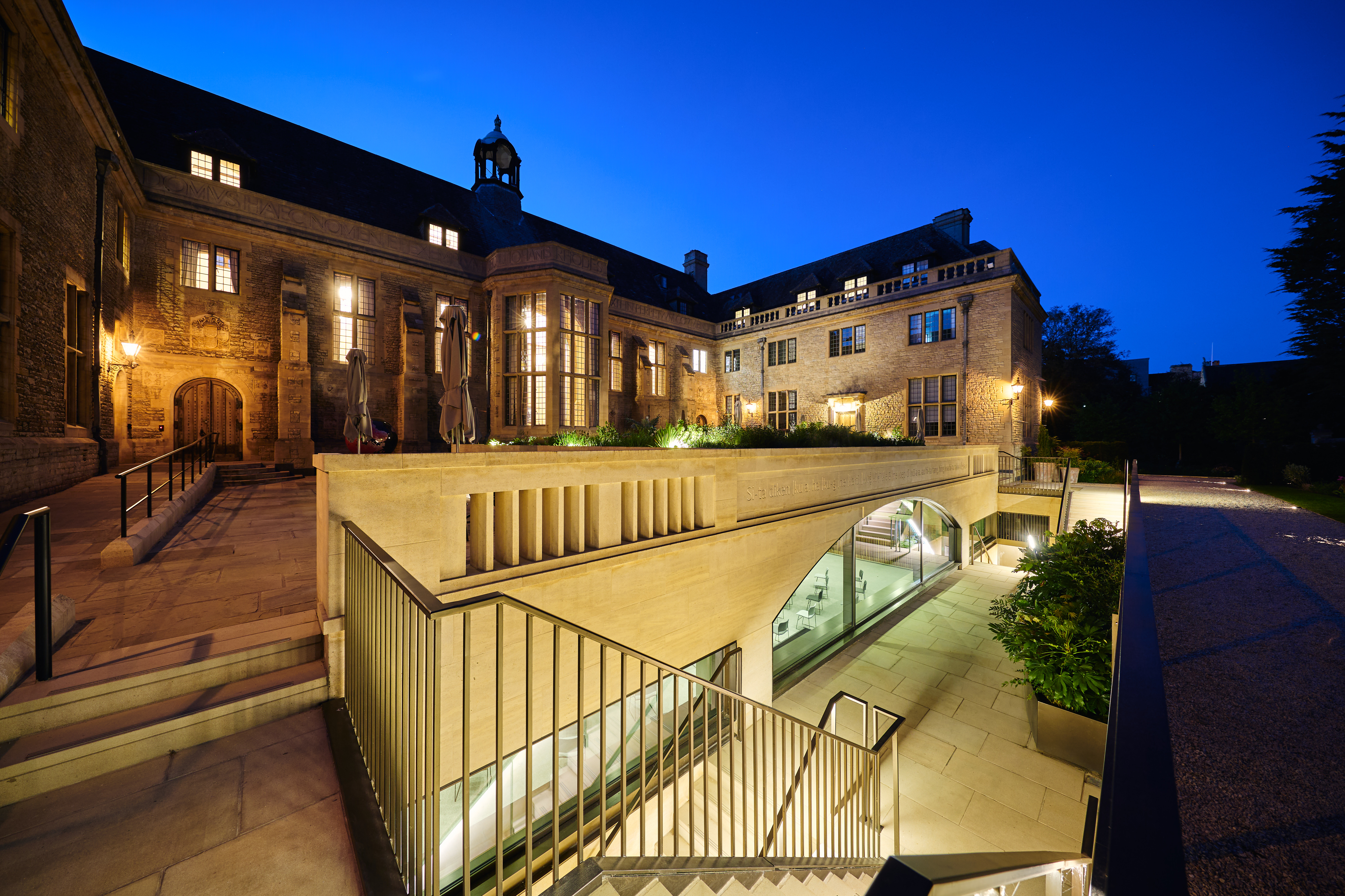 View of the Rhodes House Courtyard at night with lights coming from the windows and steps leading to the Conference Hall below. 