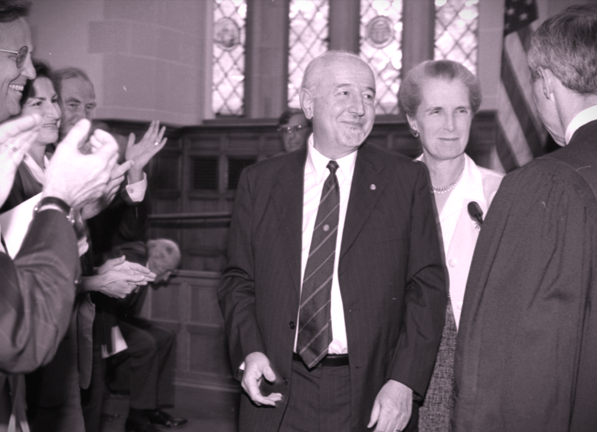 A tinted picture of Guido surrounded by people applauding as he is sworn in 