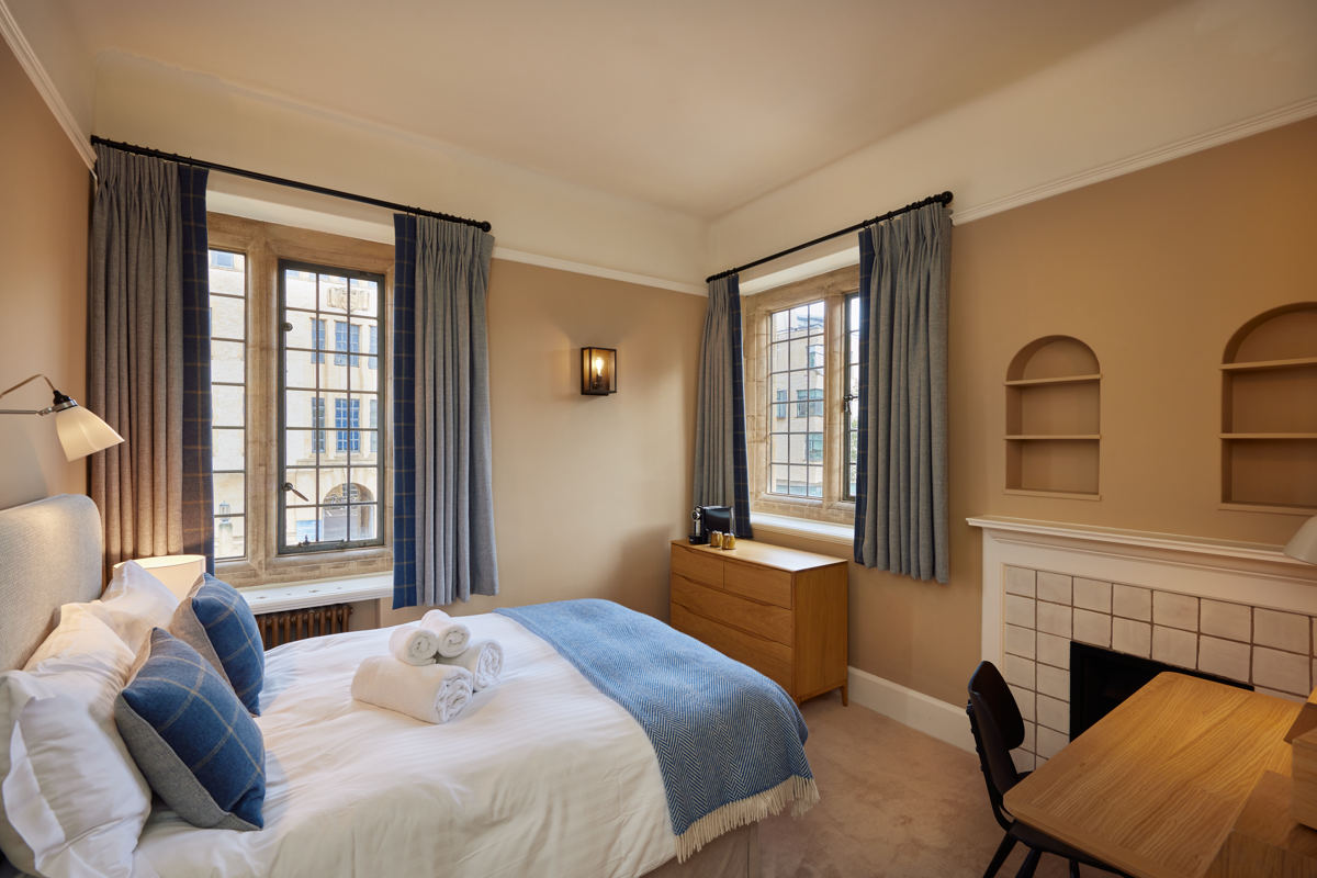 Rhodes House accommodation - double bedroom with blue blanket and blue soft furnishings; two windows with black frames. 