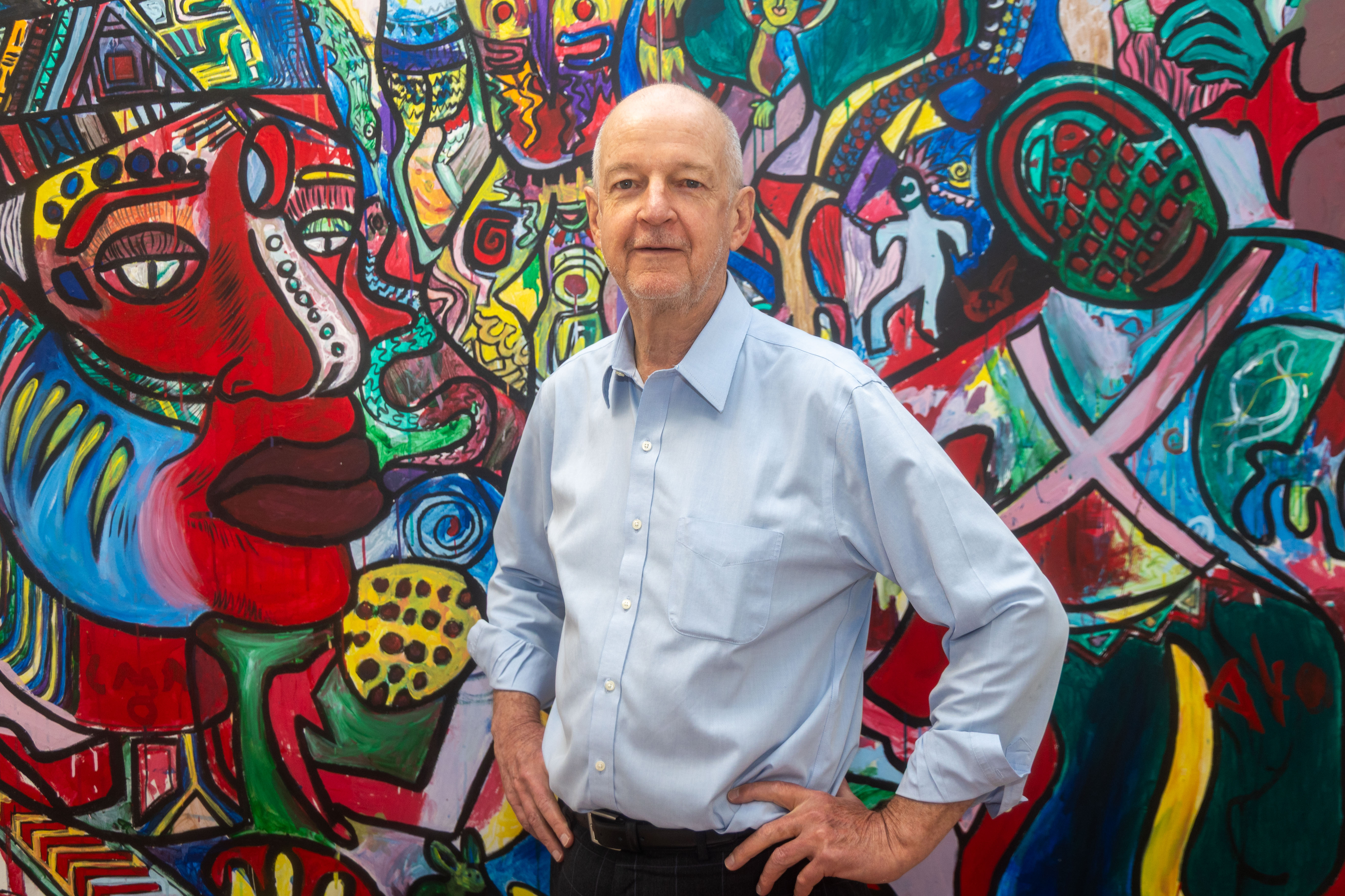 Malcolm is stood before a large paint art mural or installation. The mural depicts abstract shapes and faces.