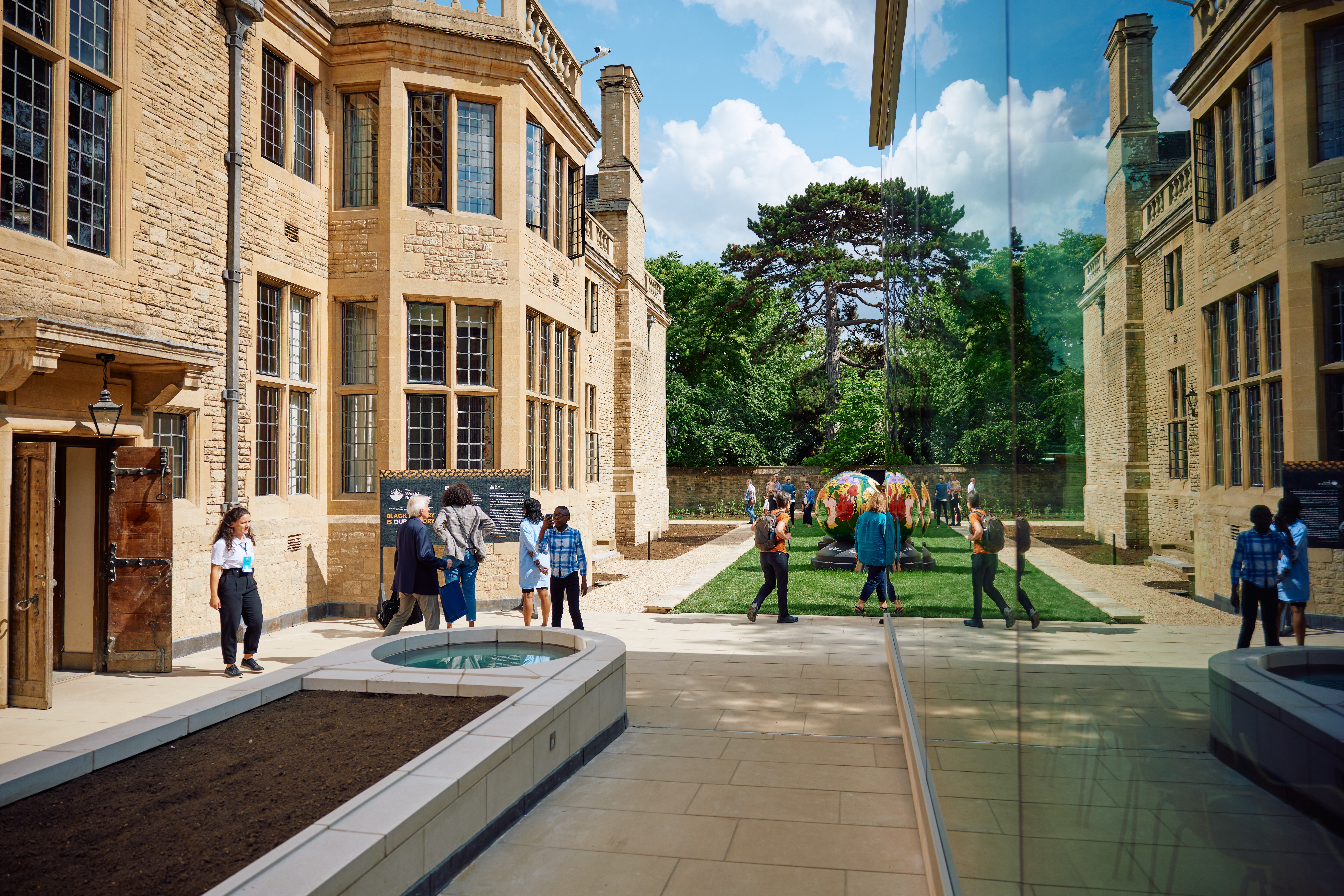 Reception guests standing in the Rhodes House west terrace with a reflection of the House visible in the wall of the Glass Pavilion.