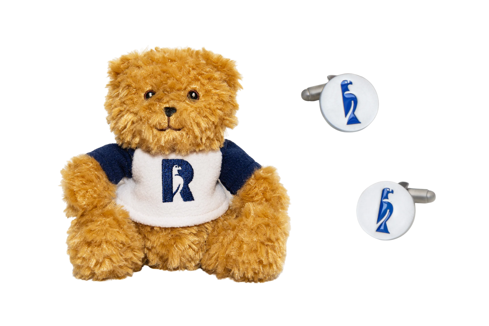 A fluffy golden-brown teddy bear wearing a white and navy t-shirt with a navy Rhodes "R" logo, beside a pair of round white cufflinks decorated with the blue Rhodes 'Zimbabwe bird' emblem.