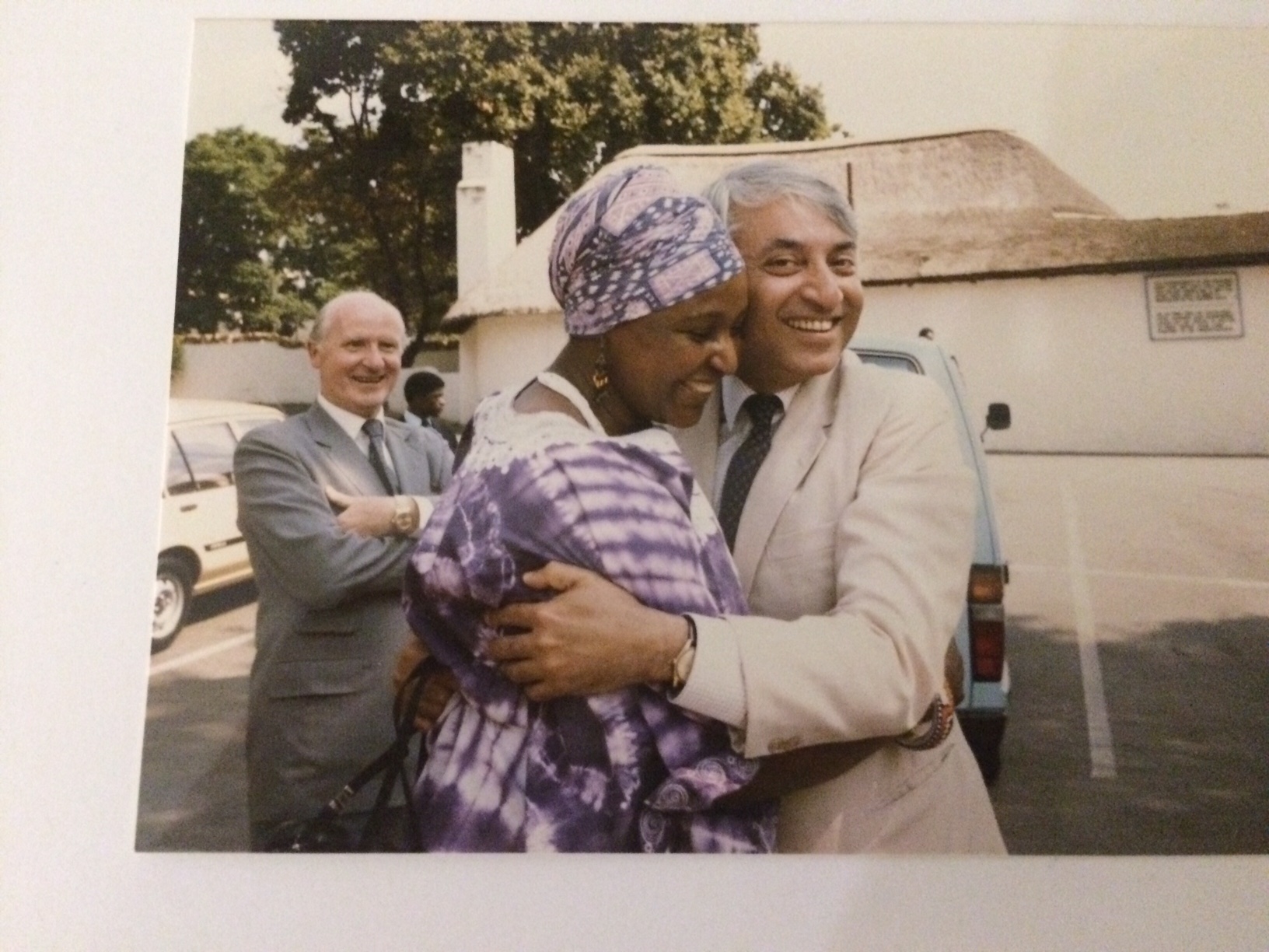 The picture shows Moni in a beige suit hugging Winnie Mandela. In the background is another man,