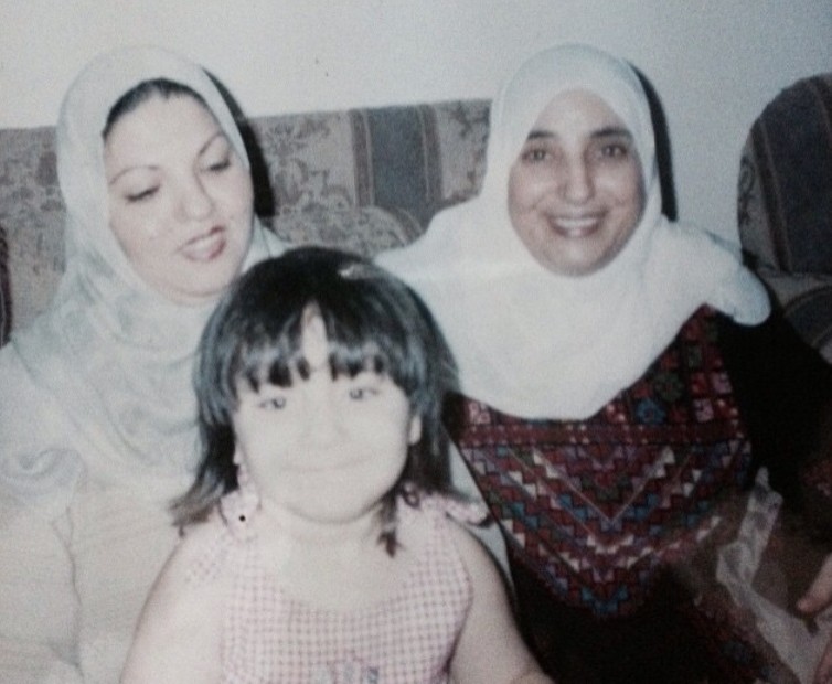An old-style photo of a child smiling next to two adult women