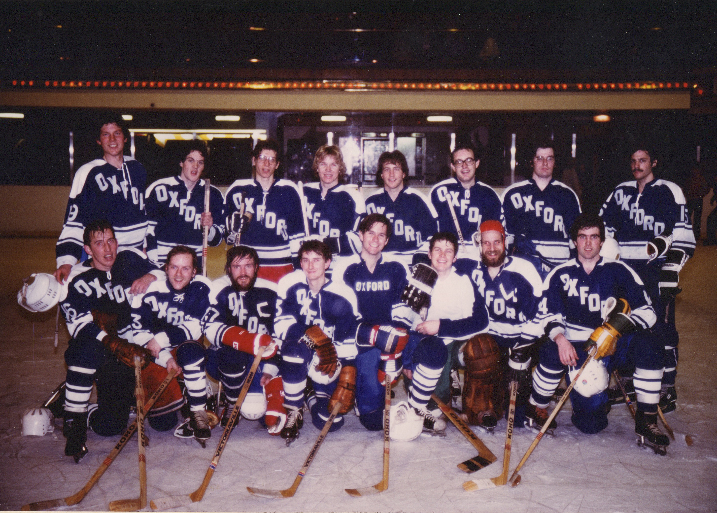 Photo of a hockey team assembled in tiers, all posing and holding their sticks out on the front-they are on an ice hockey pitch.