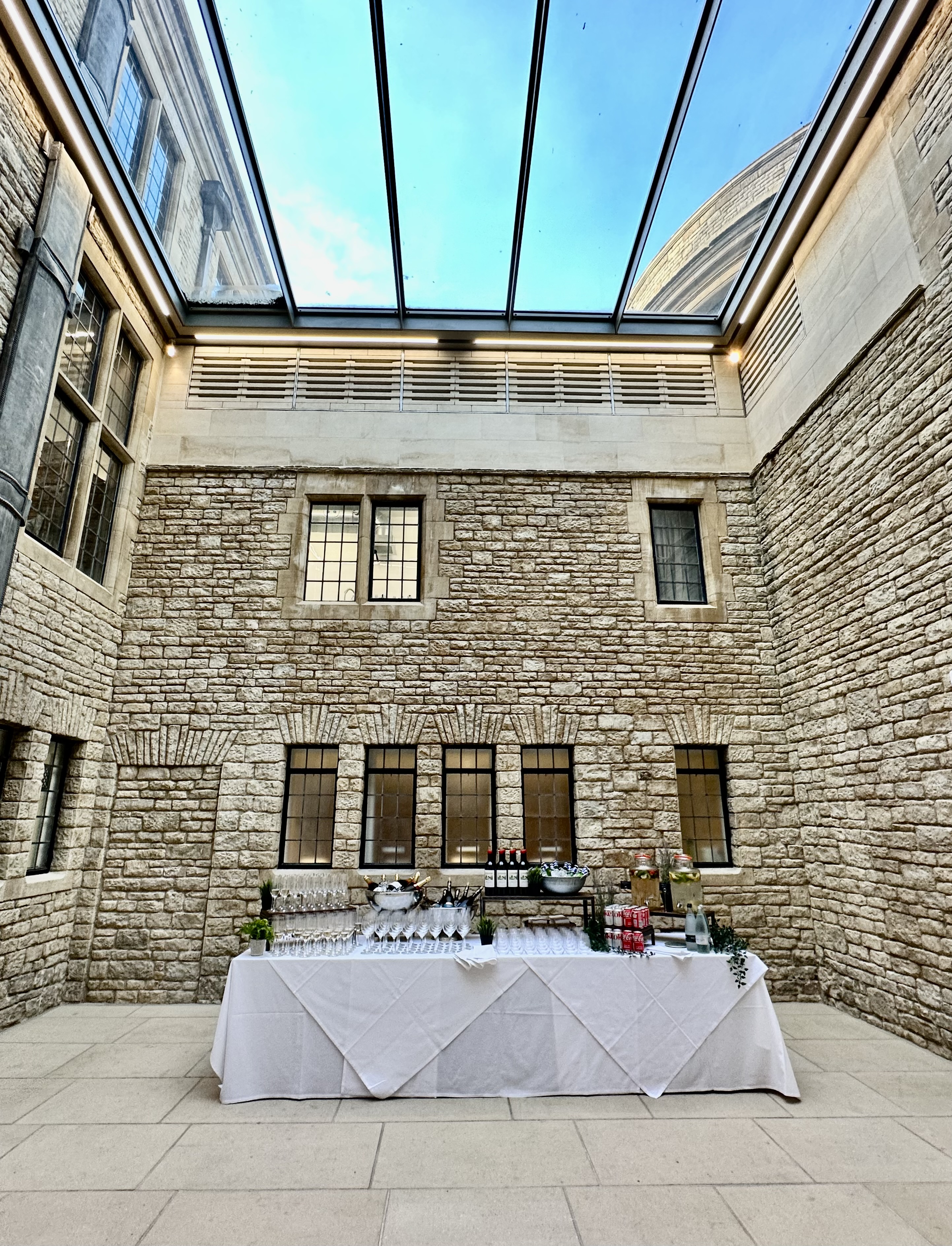 Rhodes House Lightwell with table set up for a drinks reception and blue skies visible through the glass ceiling.
