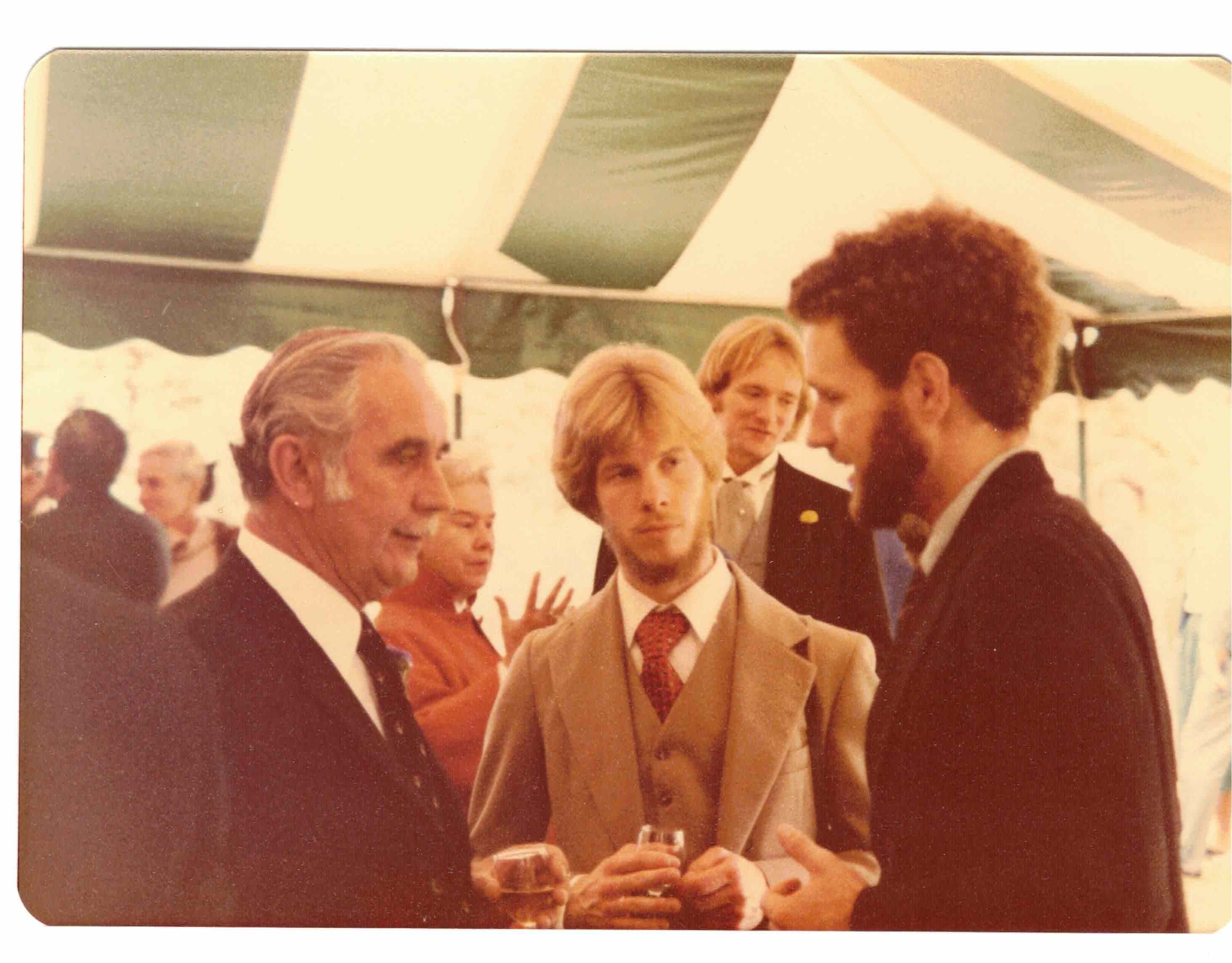 Sepia tinted wedding photo of three men talking.