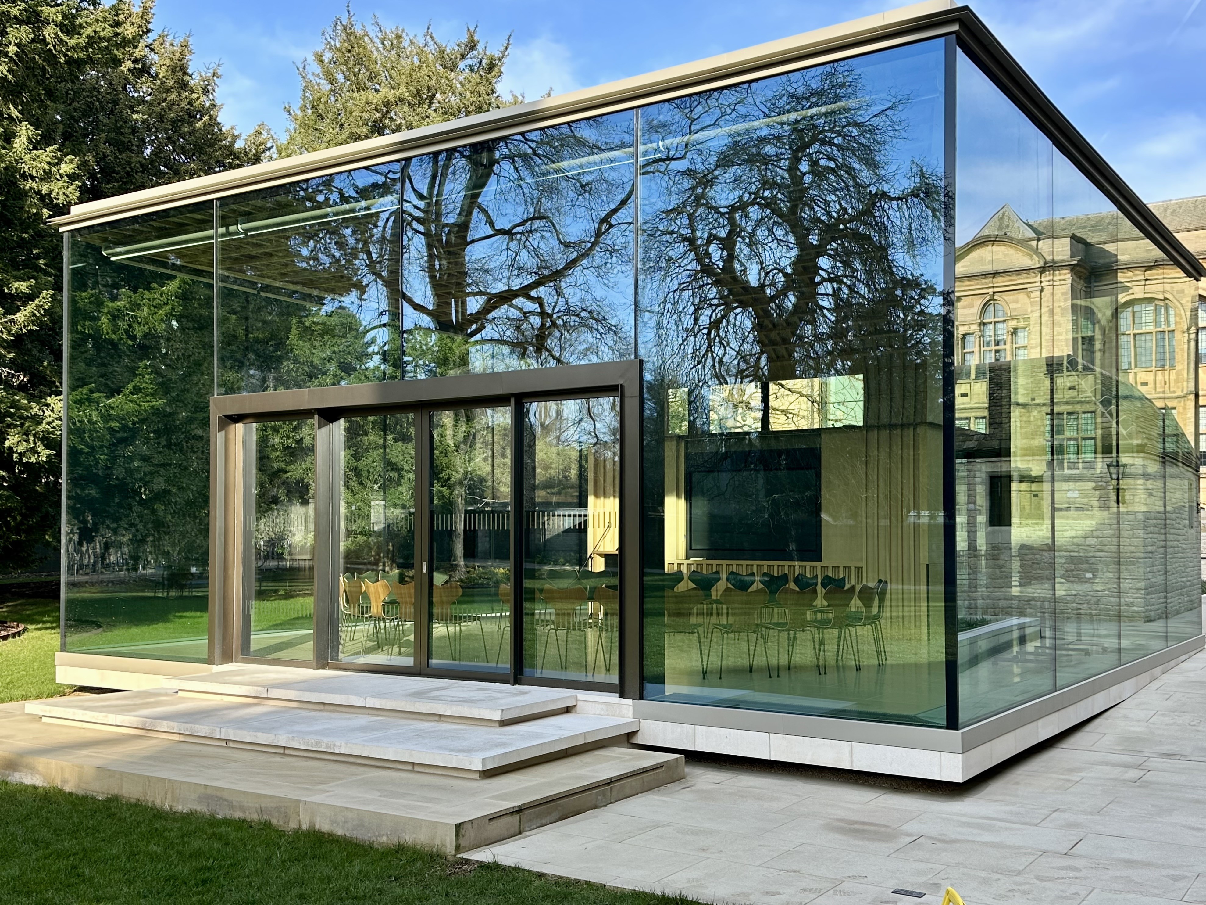 View of the Rhodes House Glass Pavilion from the West Lawn with a circle of chairs inside the room.