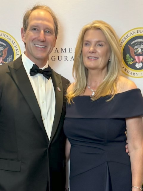 Randy and his wife pictured in an evening suit and dress, they are both posing for a camera.