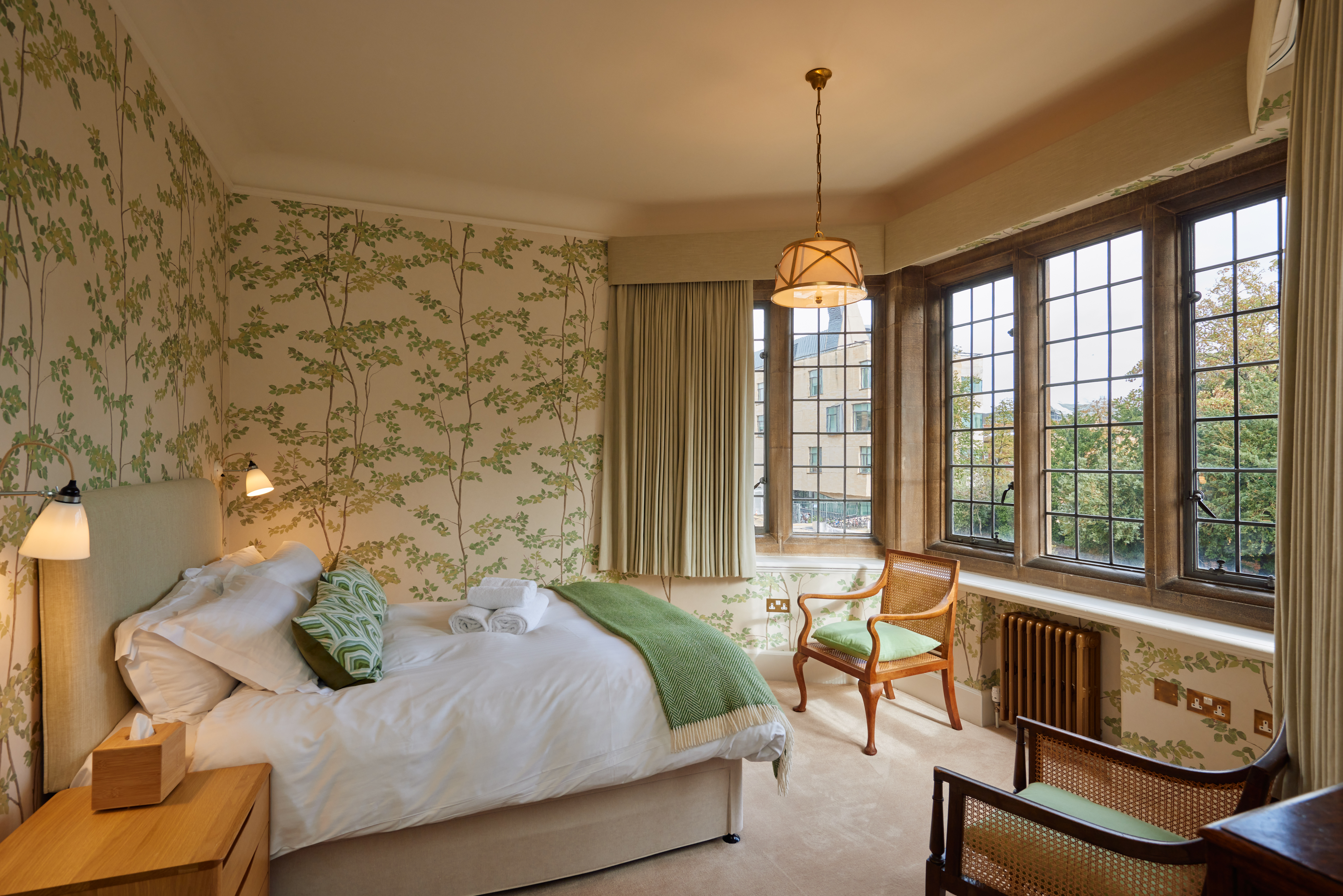 Rhodes House accommodation - double bedroom with green floral wallpaper and green soft furnishings, with a large bay window facing the bed allowing light to flood in. 