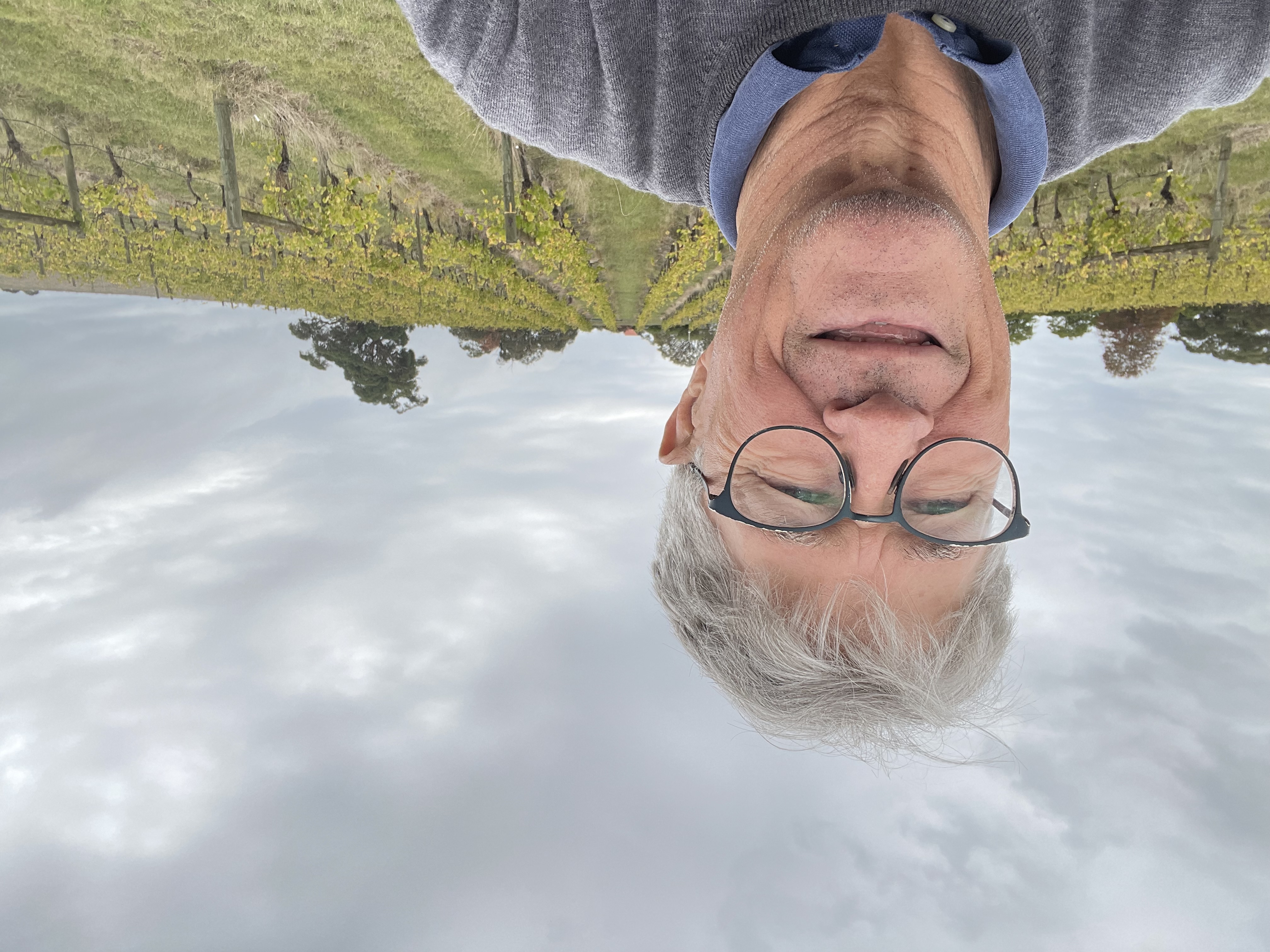 Mike taking a selfie smiling, wearing glasses. There is a farming field behind him.