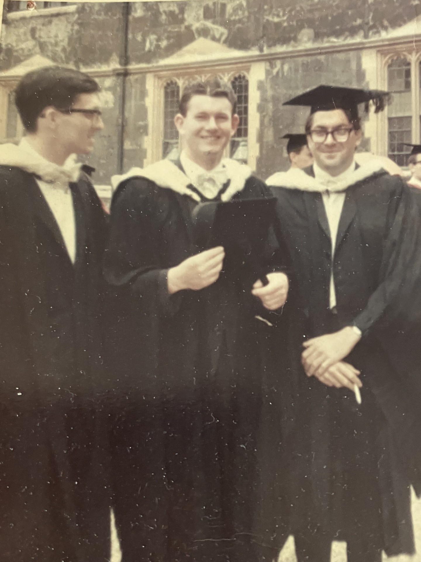 A black-and-white picture showing three men in graduation gowns. They are all smiling.