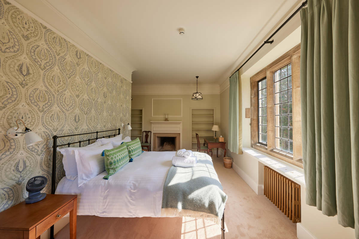 Rhodes House accommodation - double bedroom with green soft furnishings and green wallpaper, bed facing window with light flooding in.