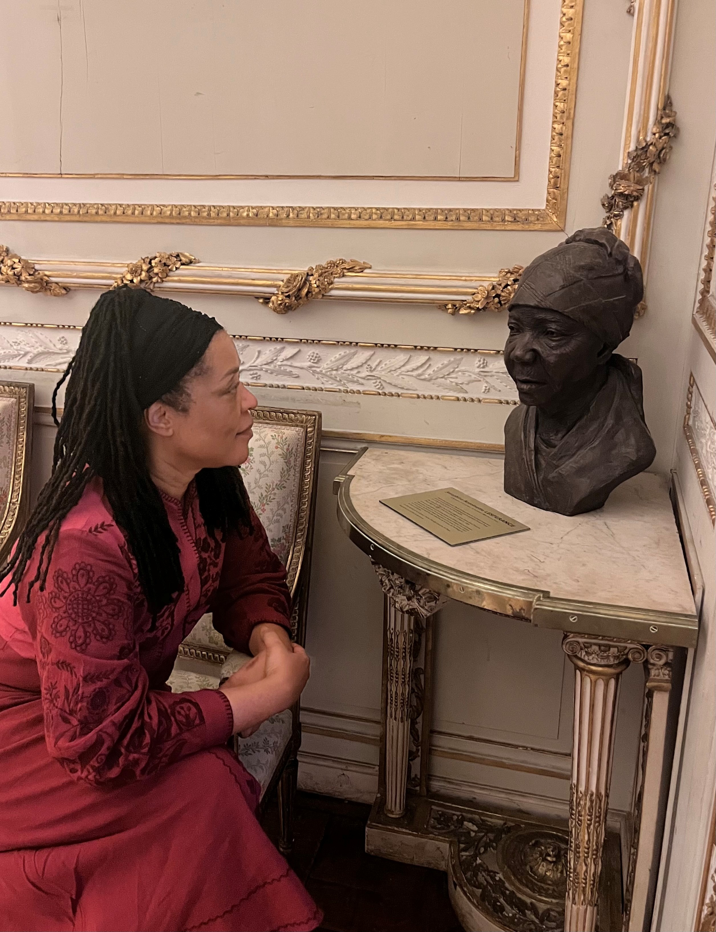 Nadine sitting on a chair looking at a bust statue