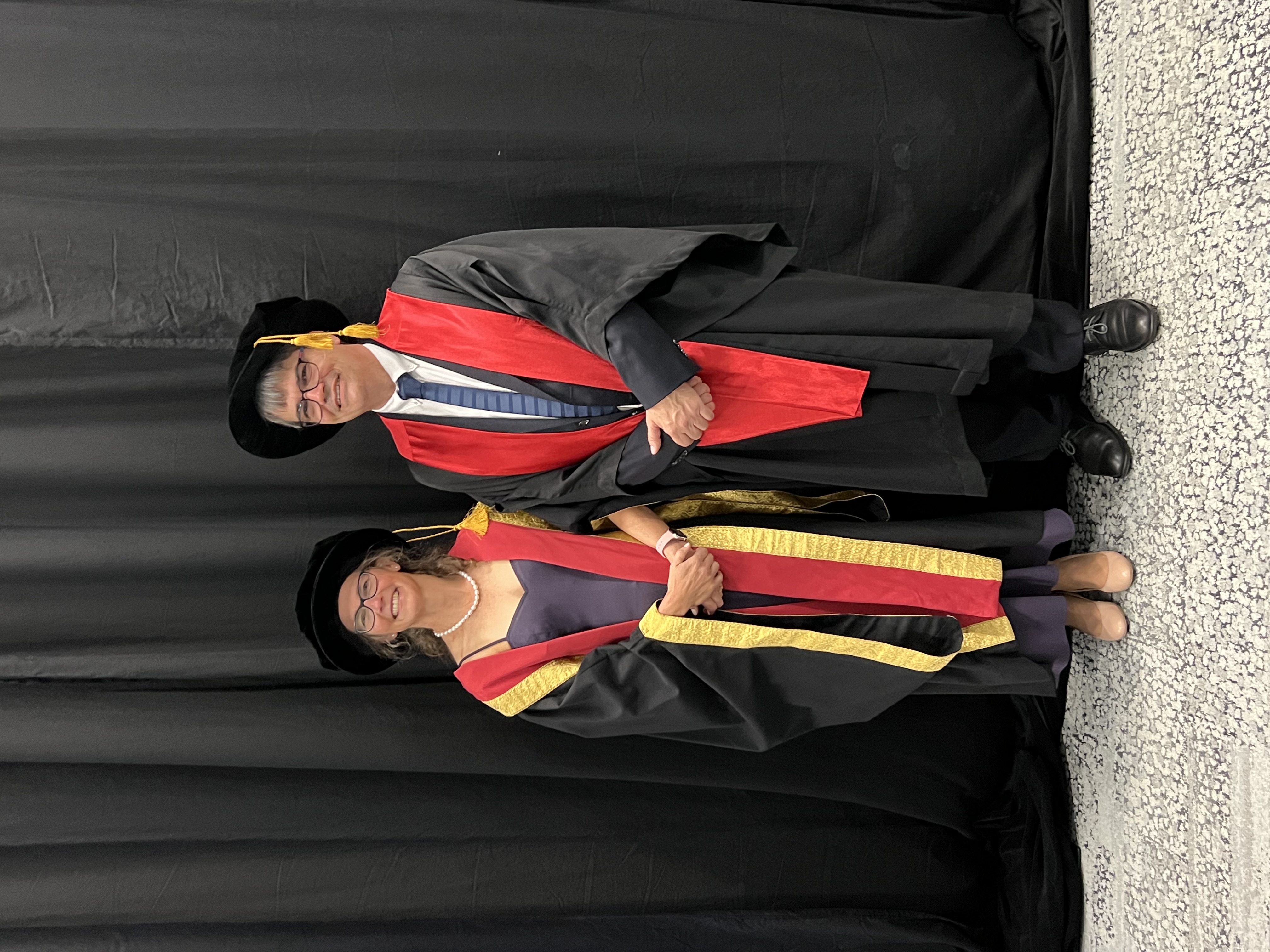 Jenny and her husband both stood in black and red gowns.