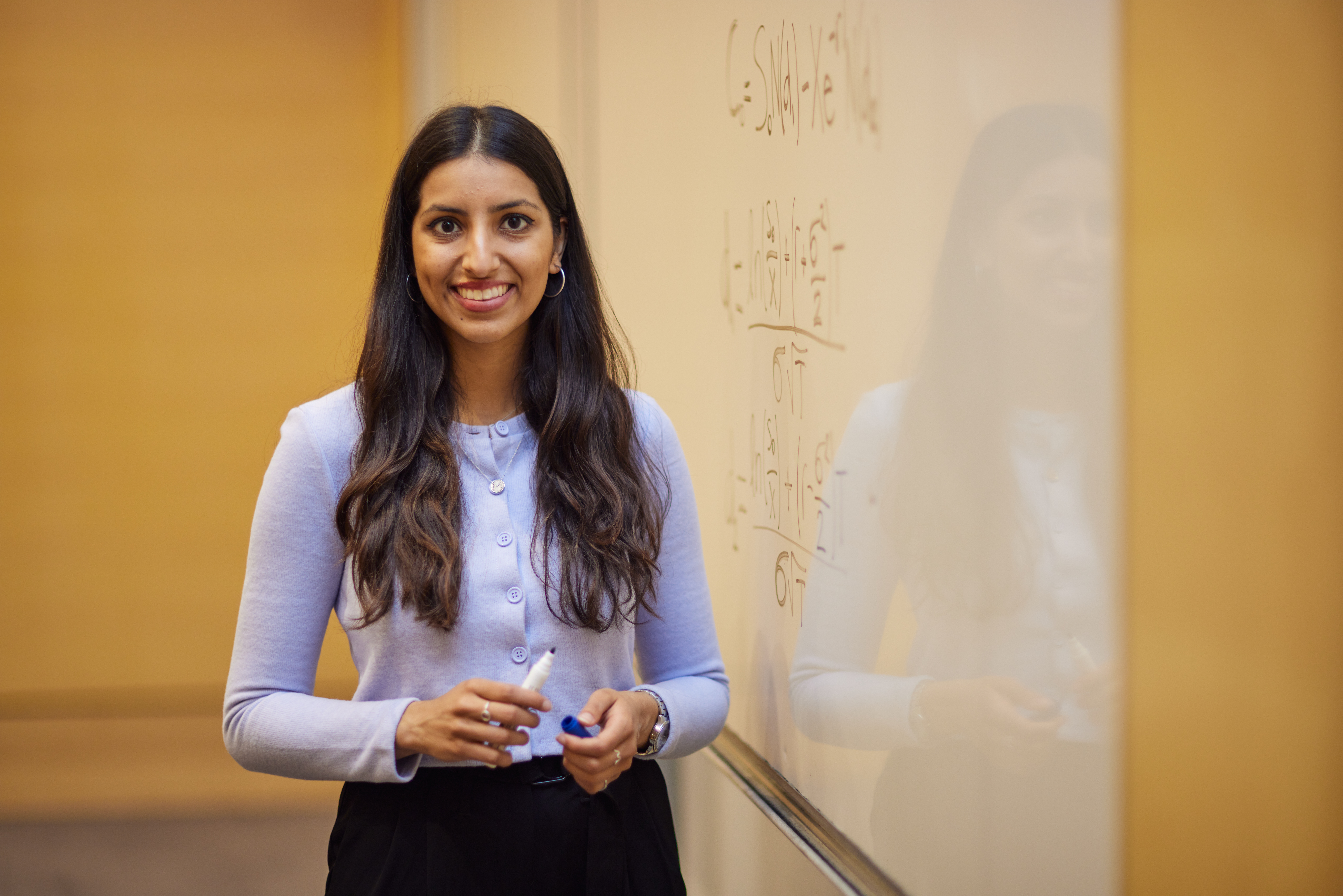 A woman Scholar smiling at the camera in front of a whiteboard with mathematical calculations