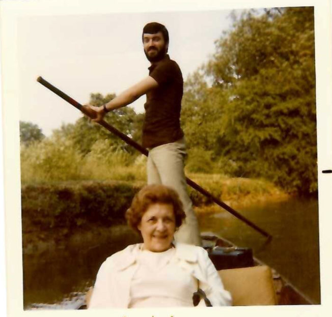 The picture shows a young Richard standing in a boat, punting. His mother is at the front of the boat. 