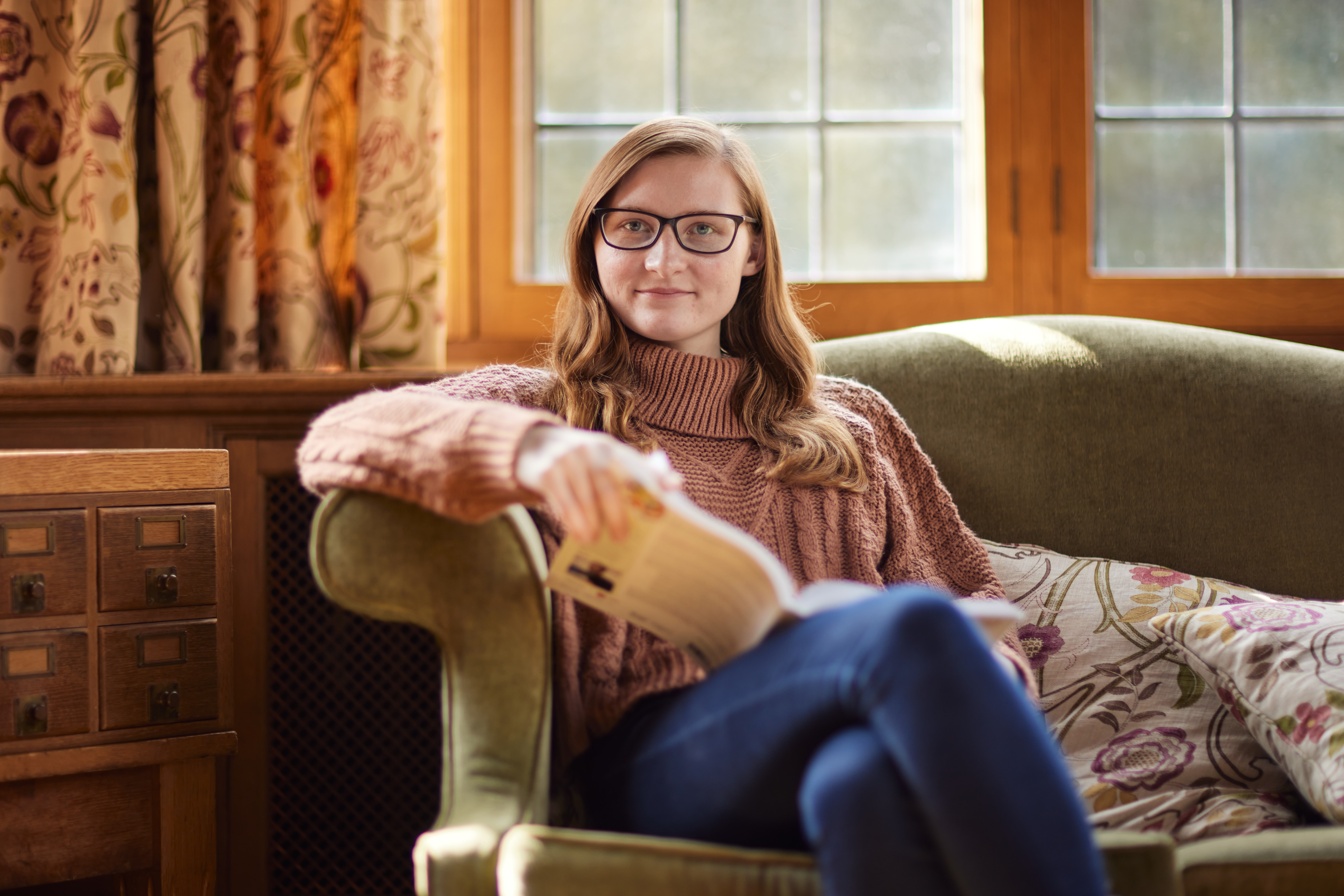 A woman sitting on a sofa in Rhodes House with the sunshine streaming in from the window behind