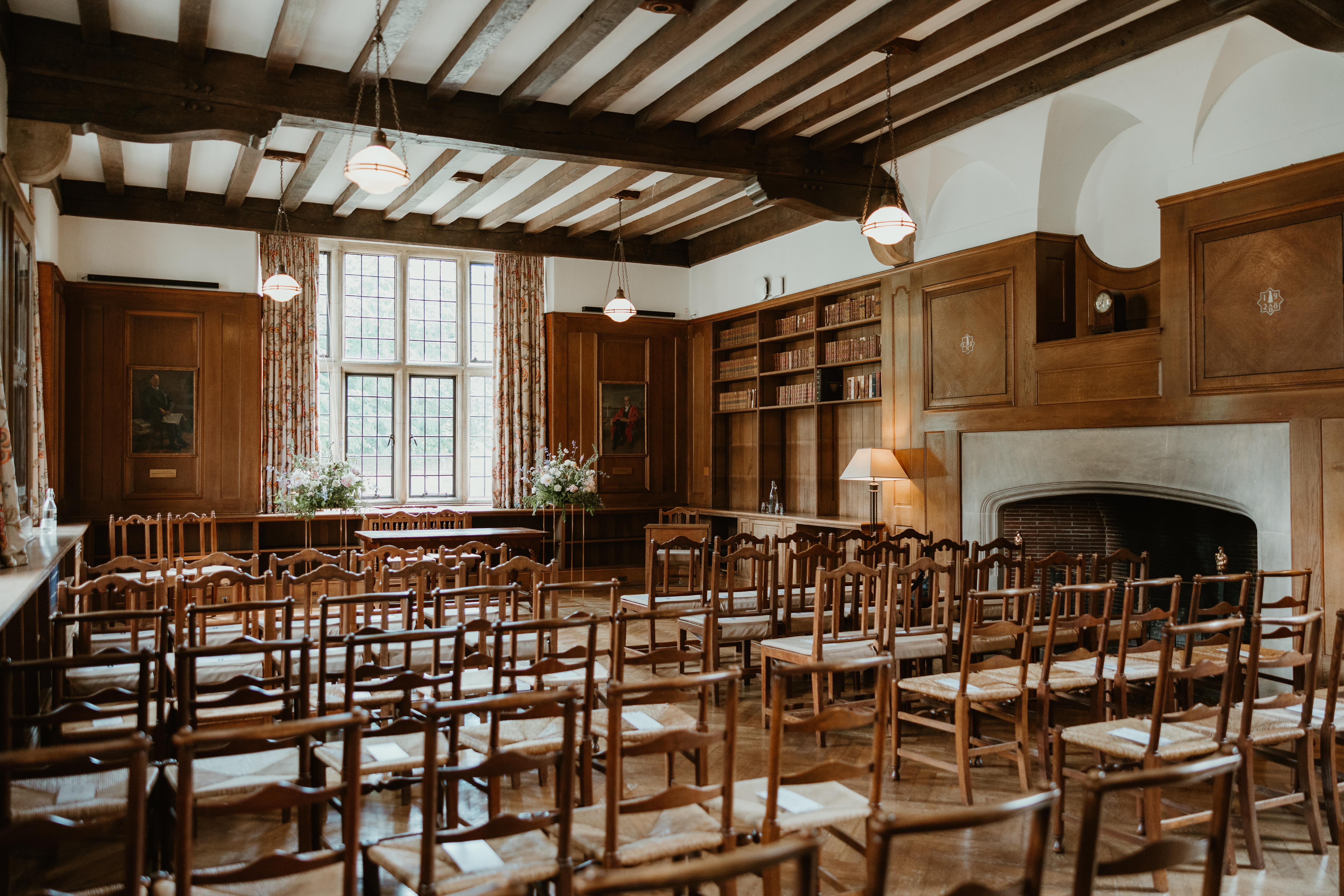 Rhodes House Beit Room set up with chairs in rows facing a window, with a large flower arrangement on either side of the window.