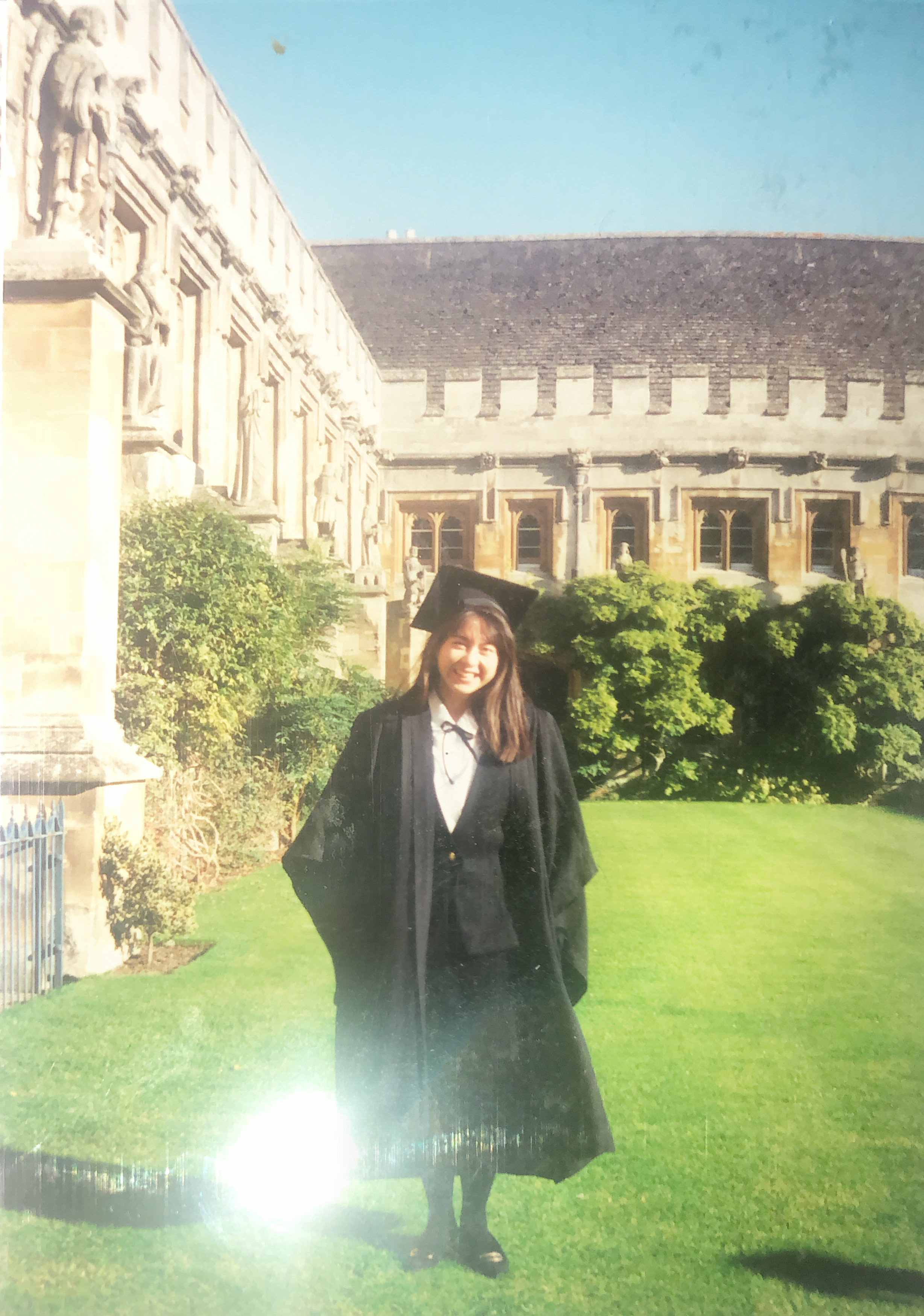 Karen in a college quad, posing in her matriculation gown and hat.