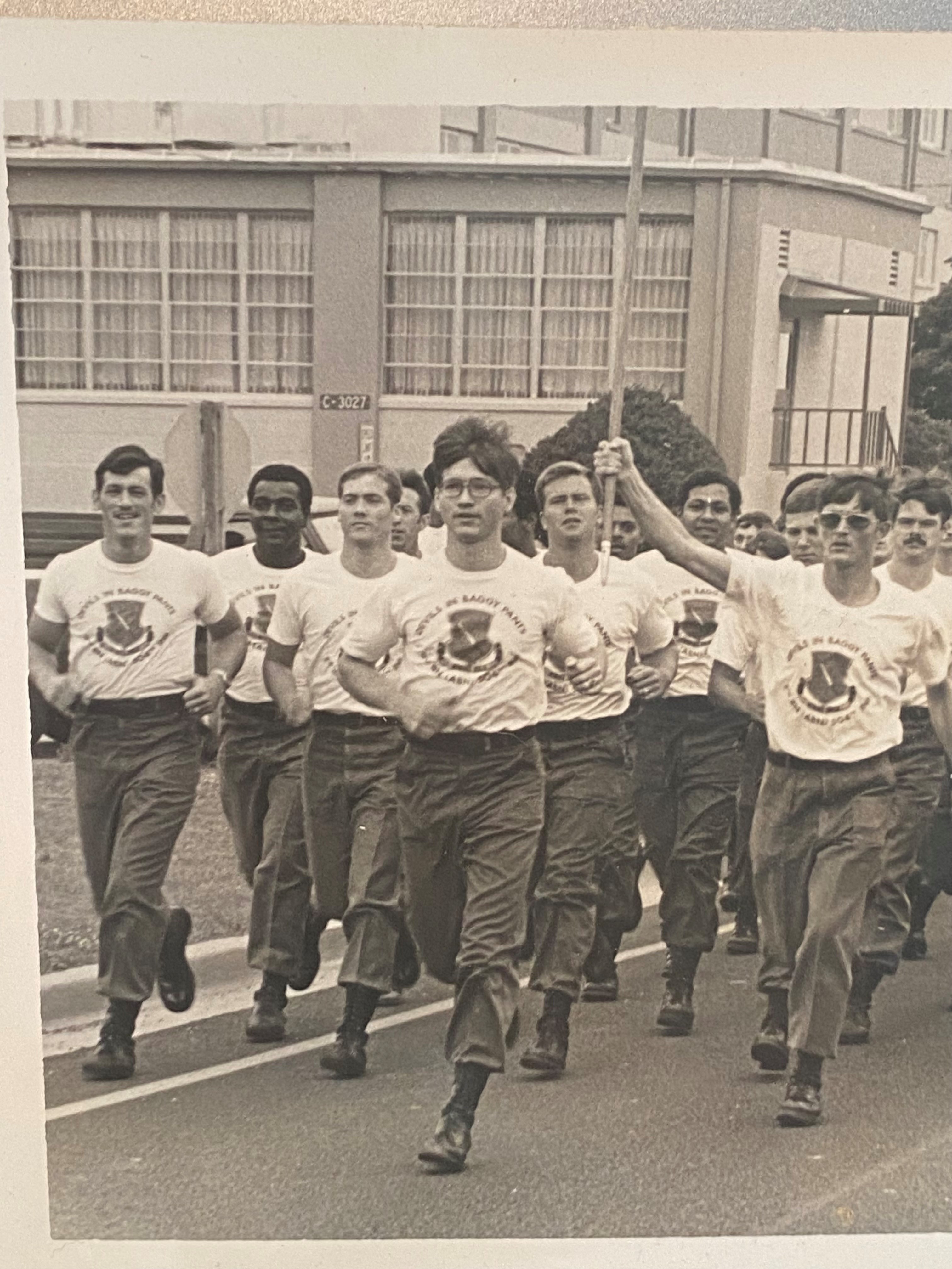 A black-and-white picture showing Jack leading a run of a group of soldiers in t-shirts, military pants and boots.