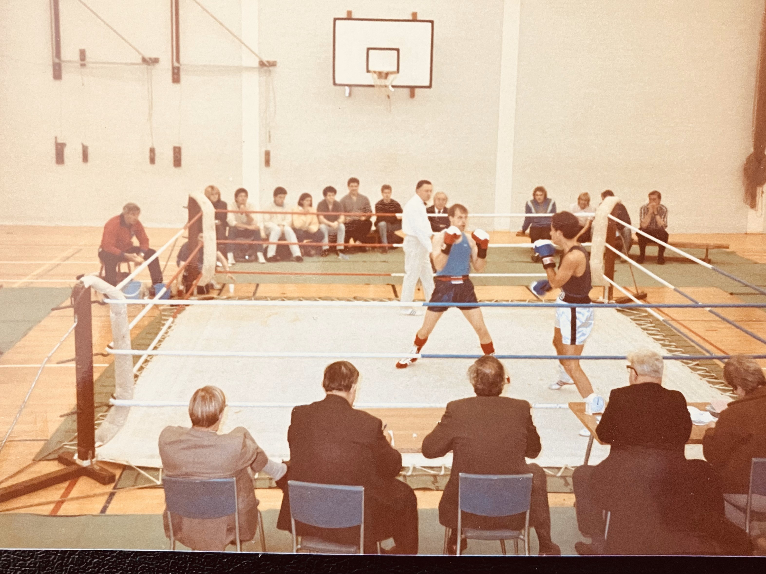 Old photo of a boxing ring, crowd watching in a sports gym and two men fighting.