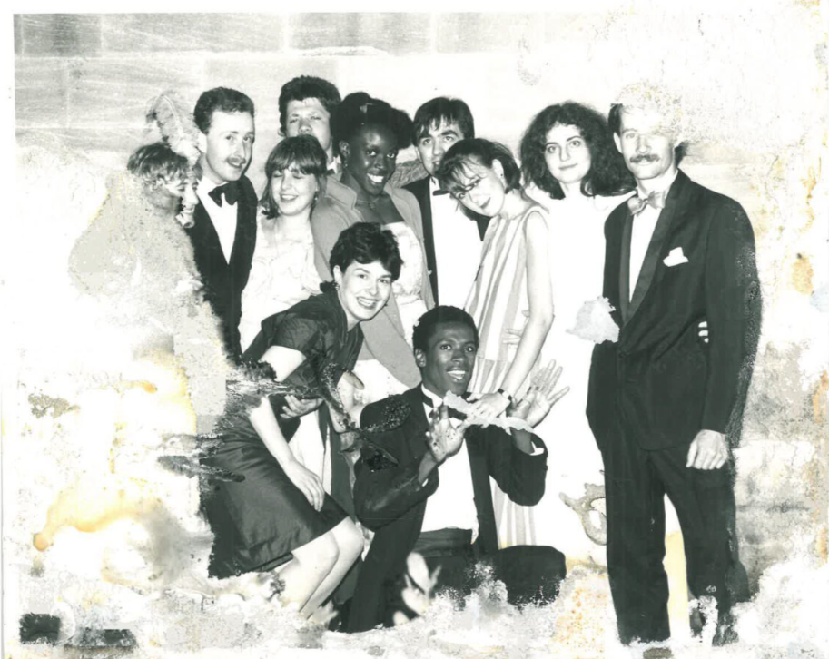 Black and white photograph of a group of students posing for a photo. they are all in suits and ball gowns. There is water ot other damage to the photo, so it is blurring away at the sides.