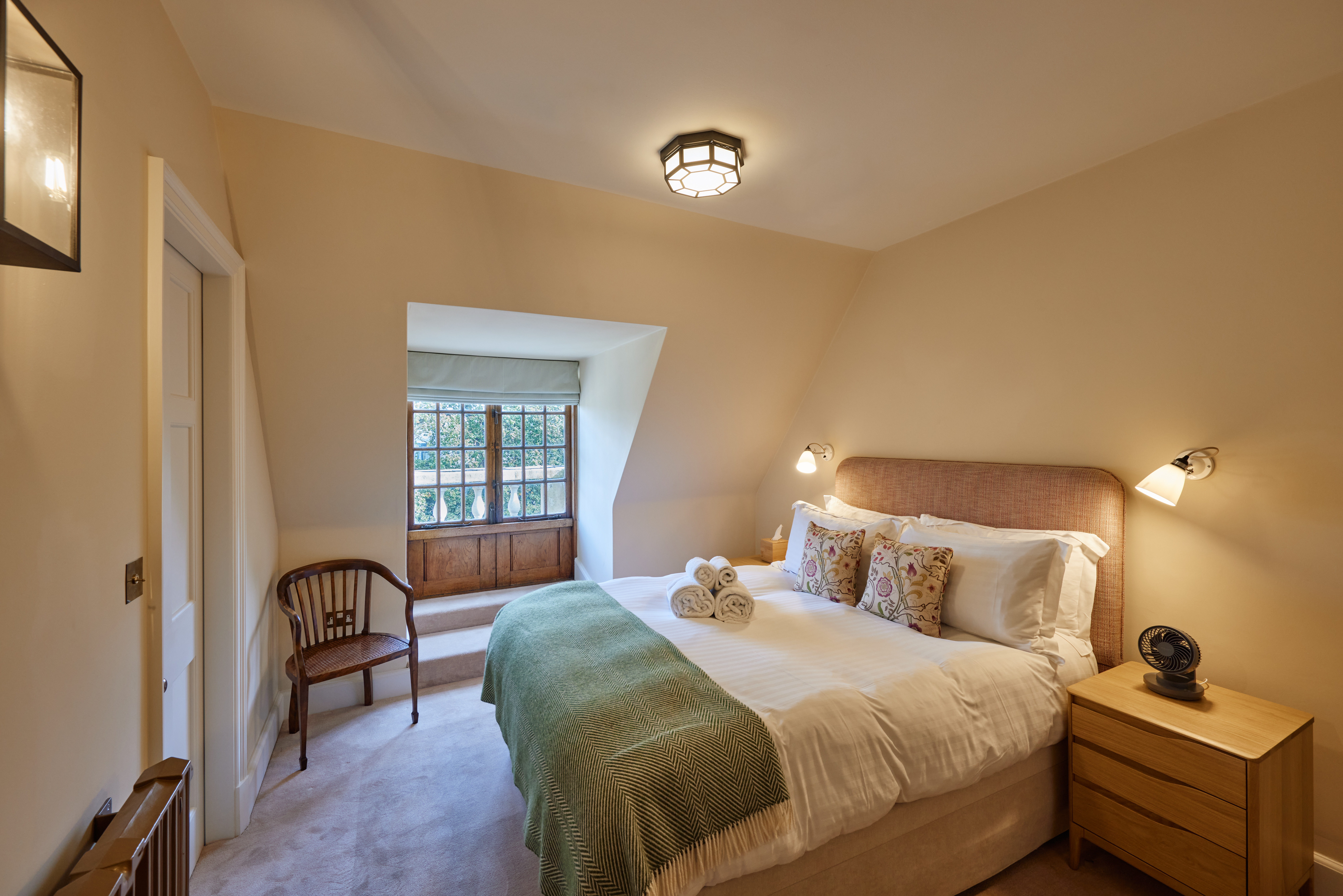 Rhodes House Accommodation - view of a double bedroom with a green blanket and beige walls, soft daylight coming through the window.