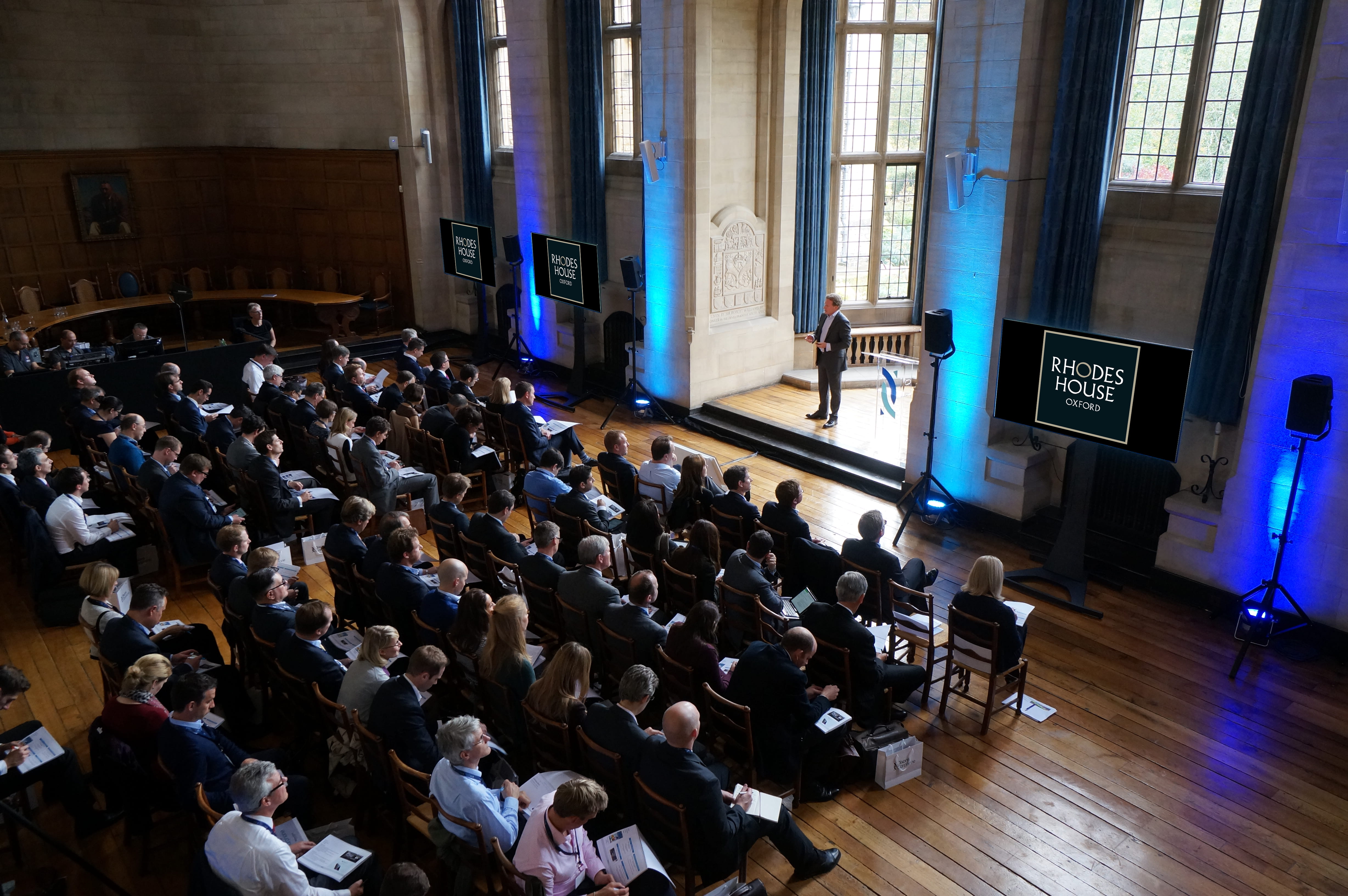 Rhodes House McCall MacBain Hall conference with delegates facing the speaker in the bay window, with screens on either side.