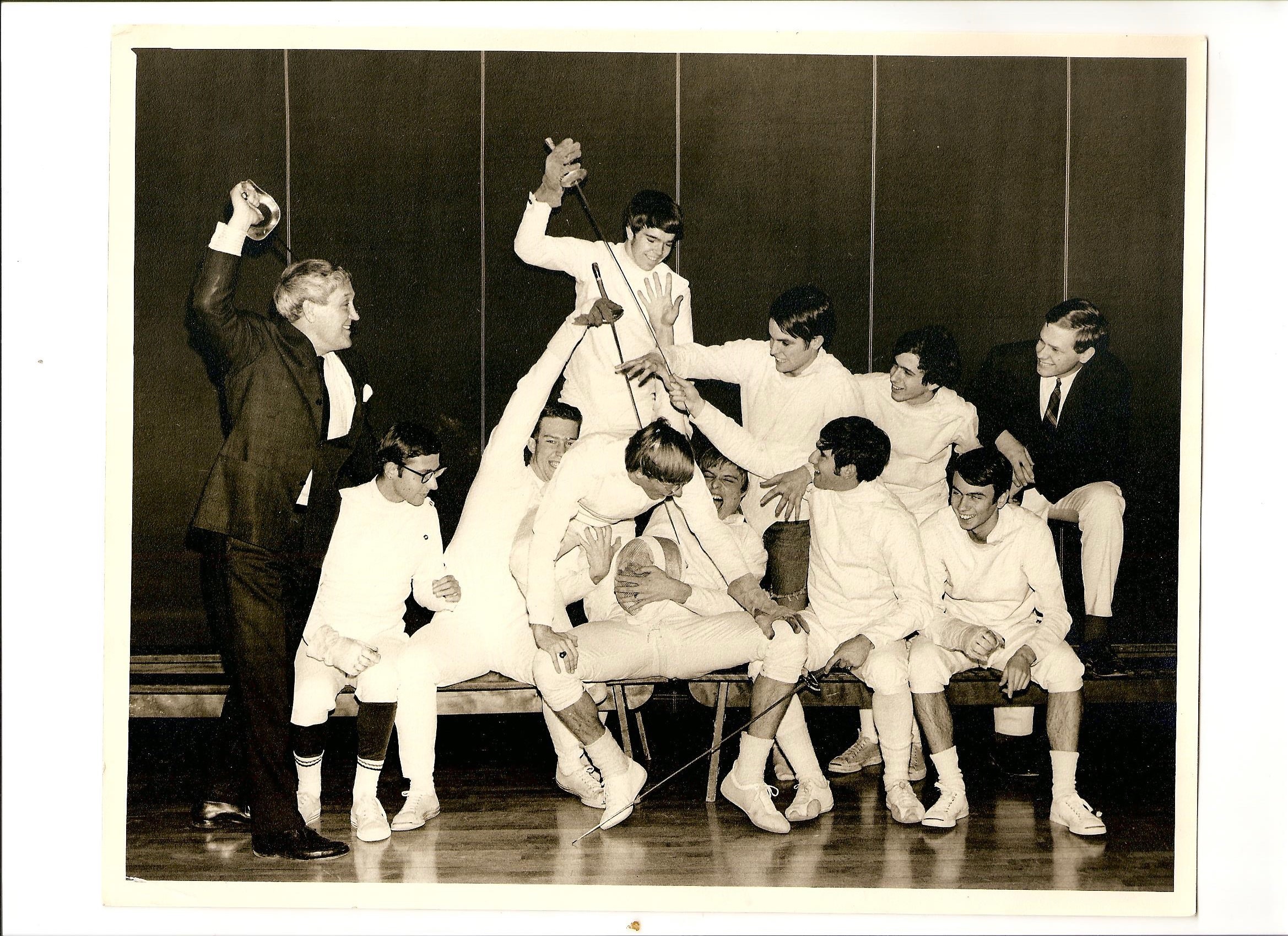 Black and white photo of group of young men fencing, wearing white.