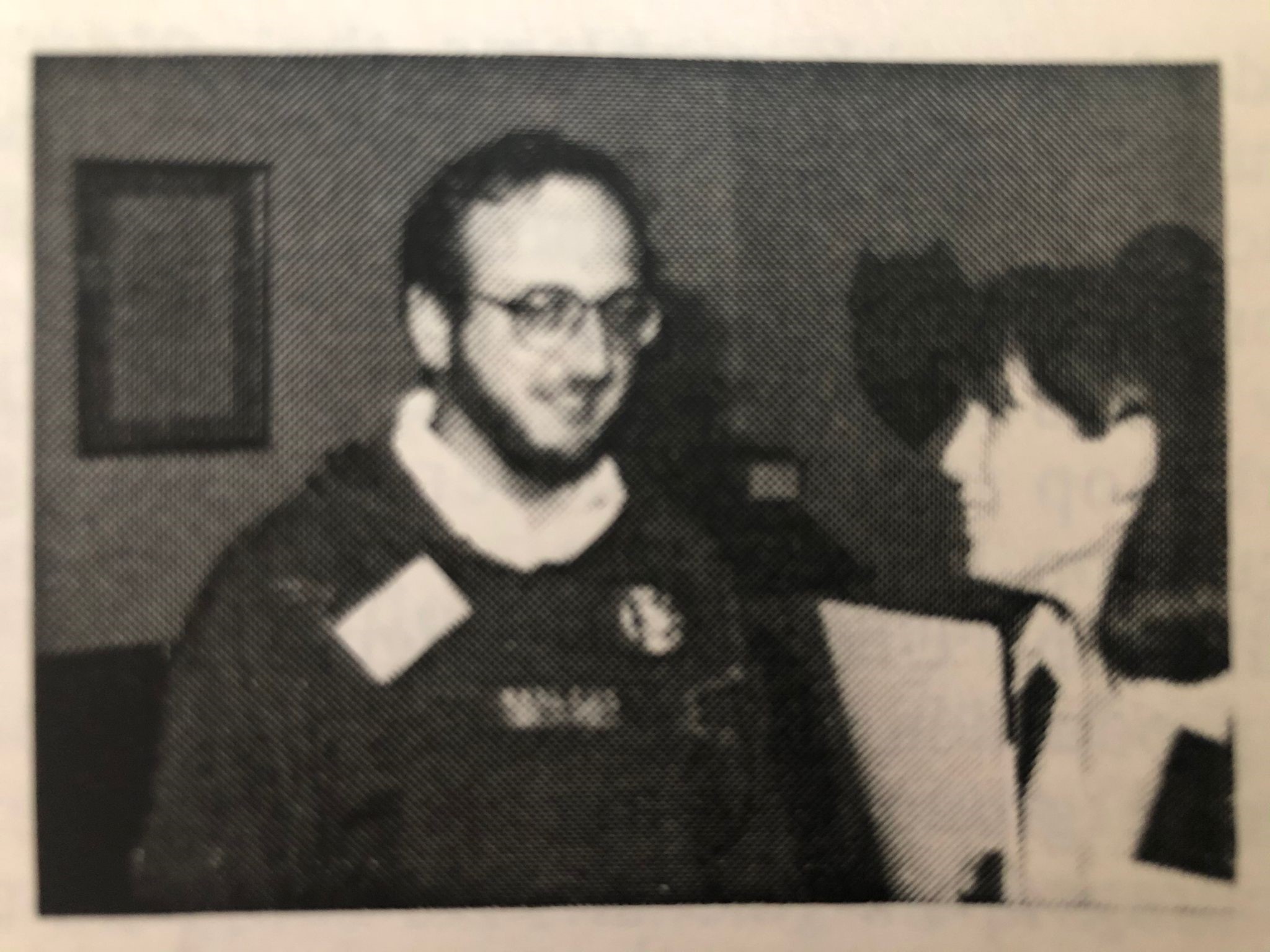 A black-and-white picture of Laurance in a jumper, talking to a woman 