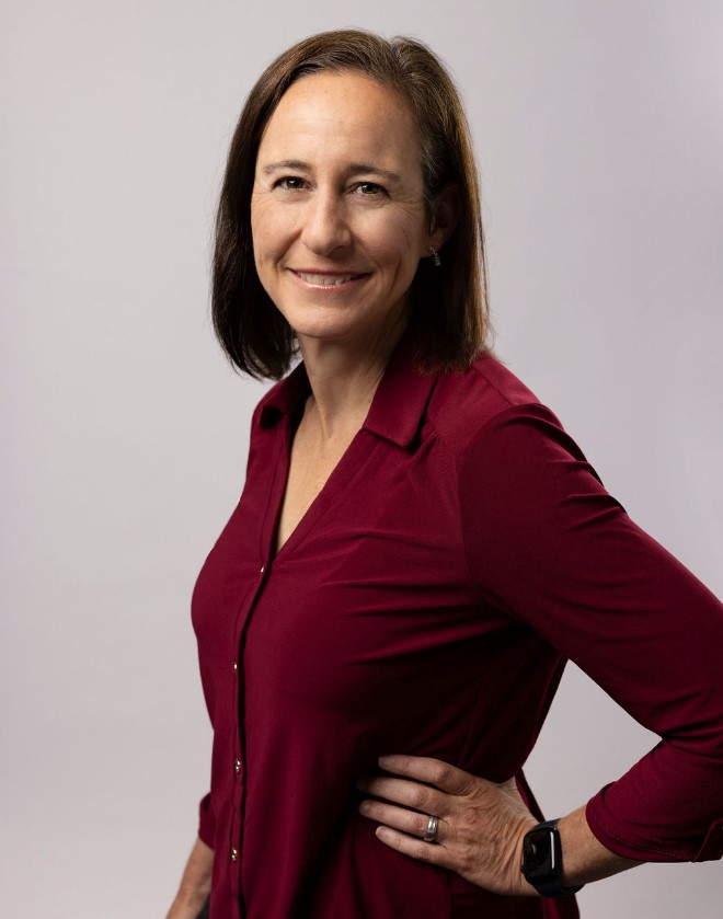 Jane stood, wearing a burgundy shirt, with her left arm against her hip and smiling into the camera.